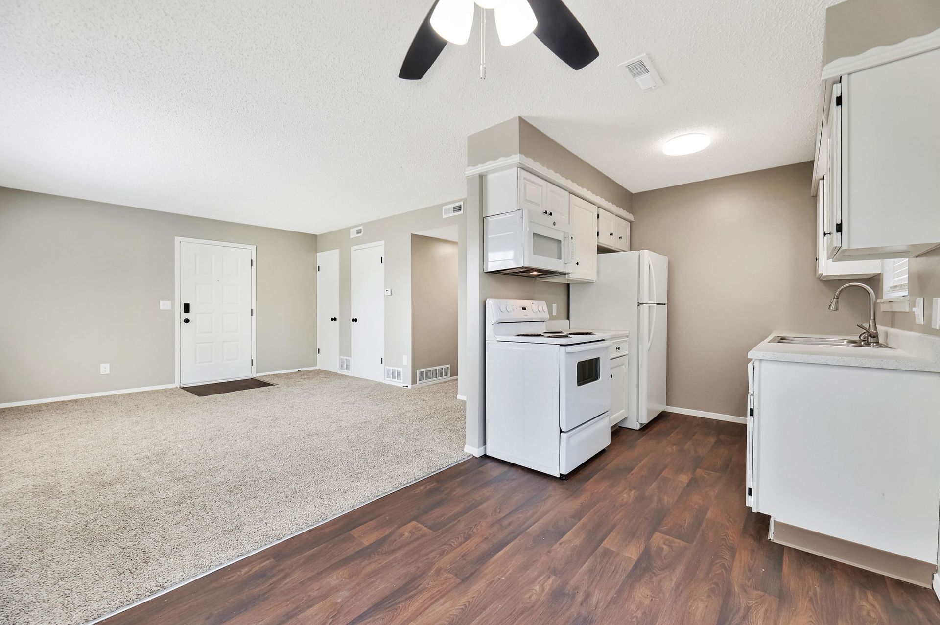 A kitchen with white appliances and a ceiling fan