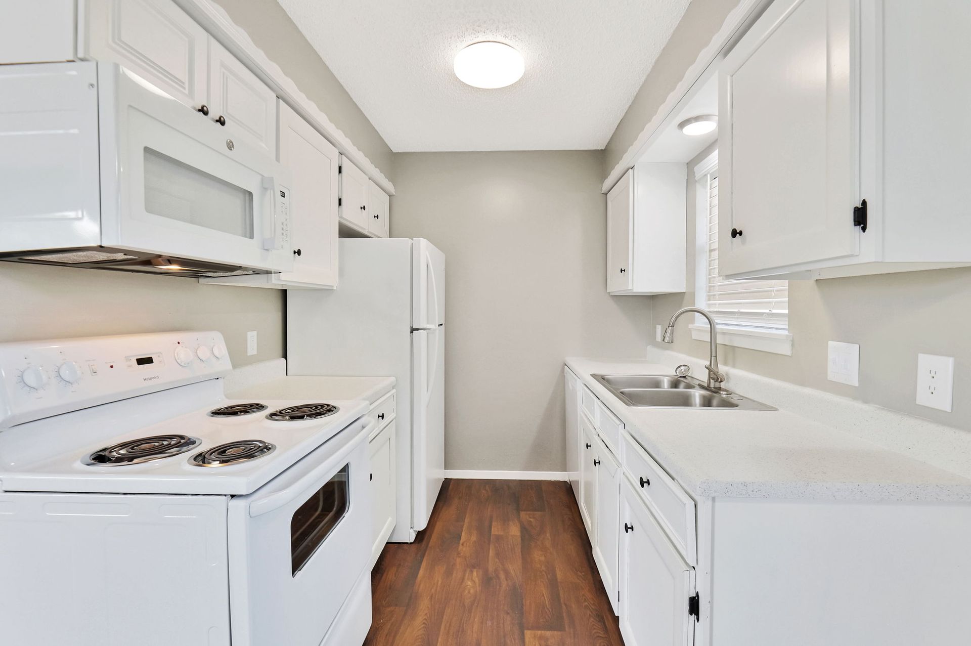 A kitchen with white cabinets , a stove , a refrigerator , and a sink.