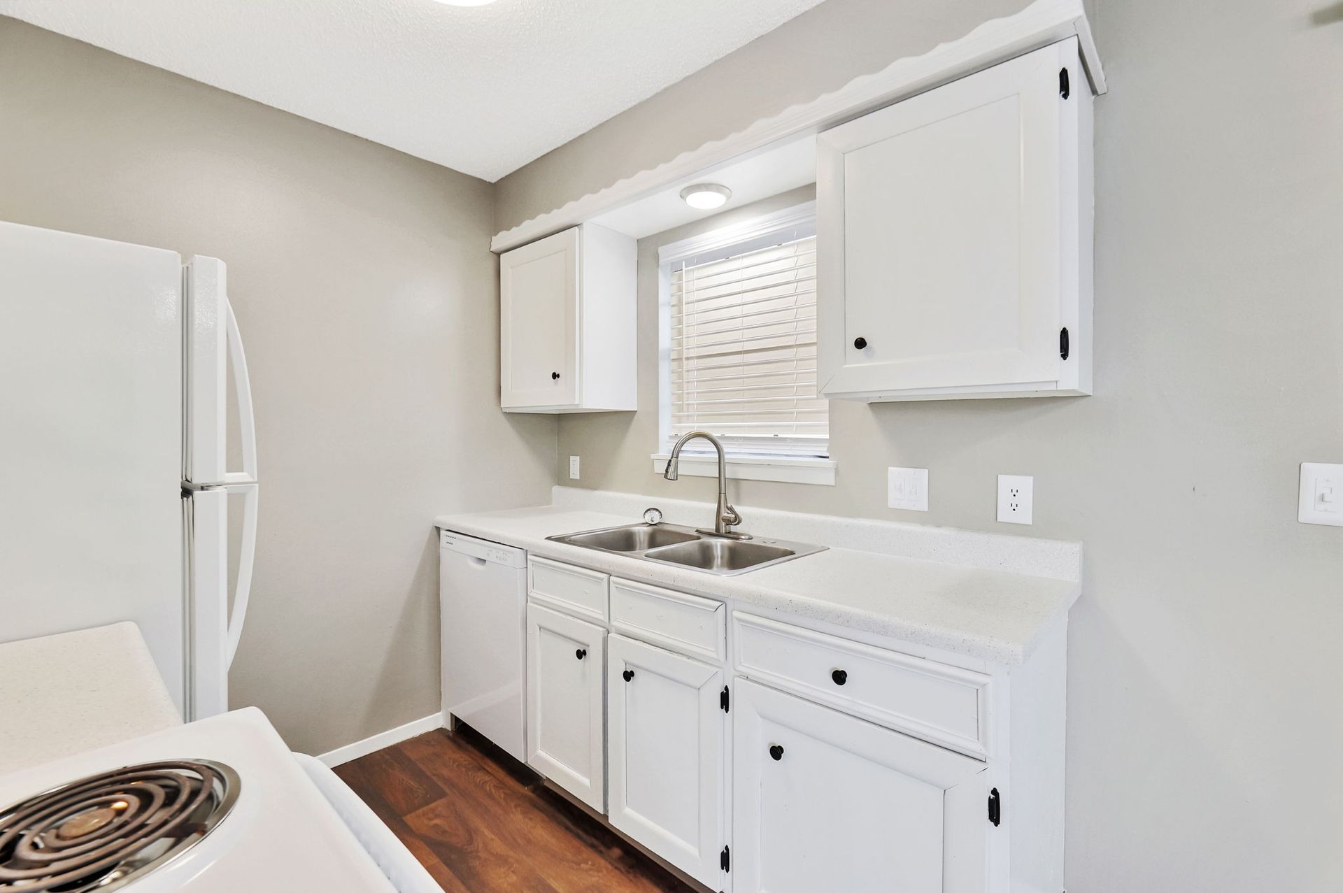 A kitchen with white cabinets , a stove , a refrigerator , a sink and a window.