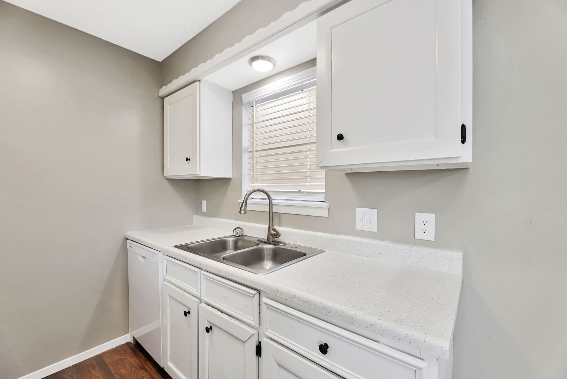 A kitchen with white cabinets , a sink , and a window.