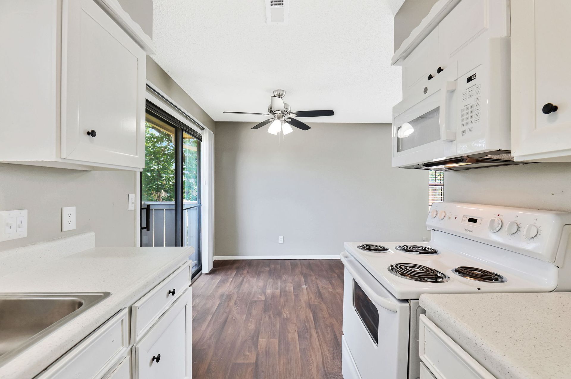 A kitchen with white cabinets , a stove , a sink , and a microwave.