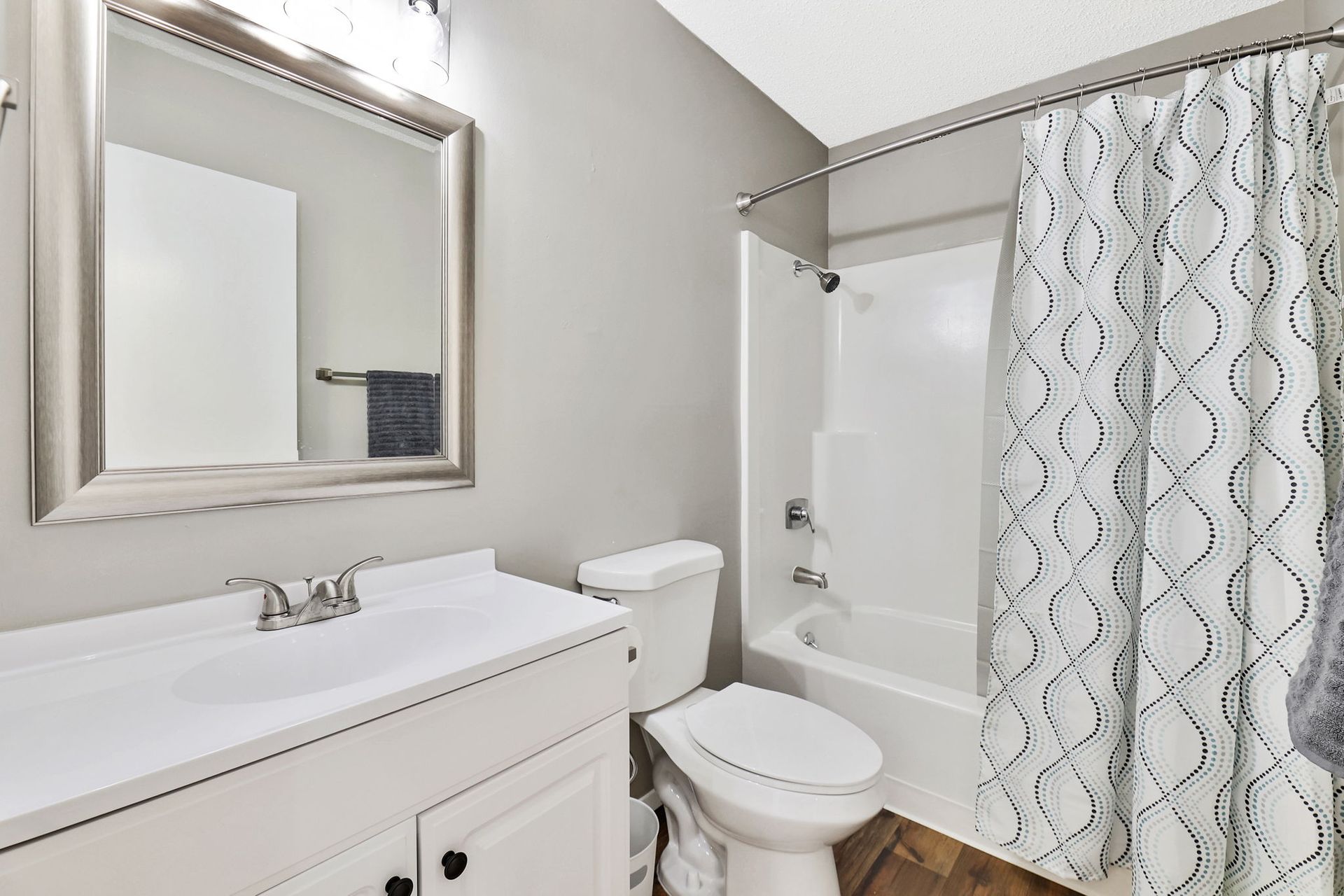 A bathroom with a toilet , sink , mirror and shower curtain.