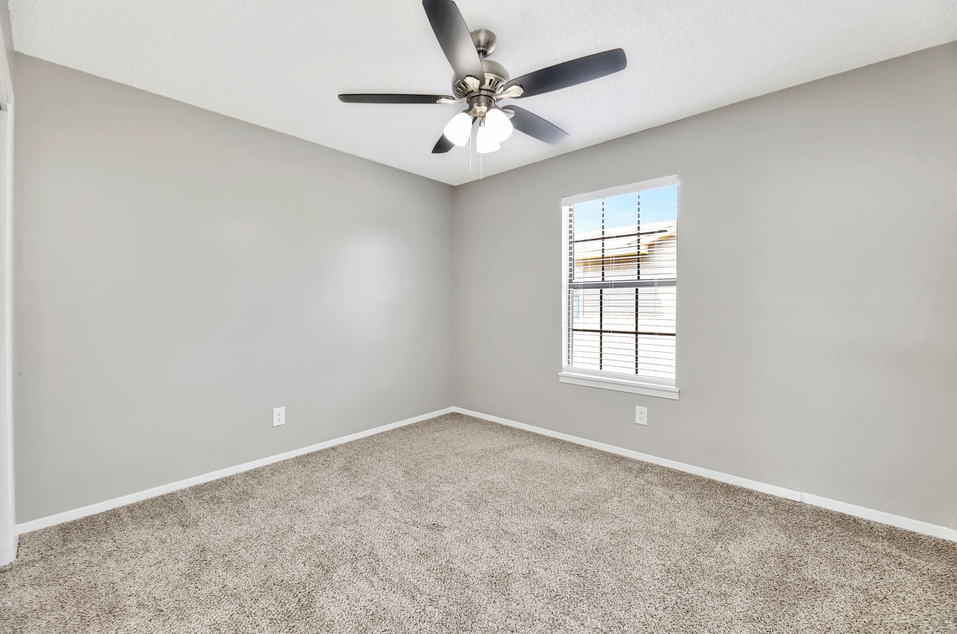 An empty bedroom with a ceiling fan and a window.