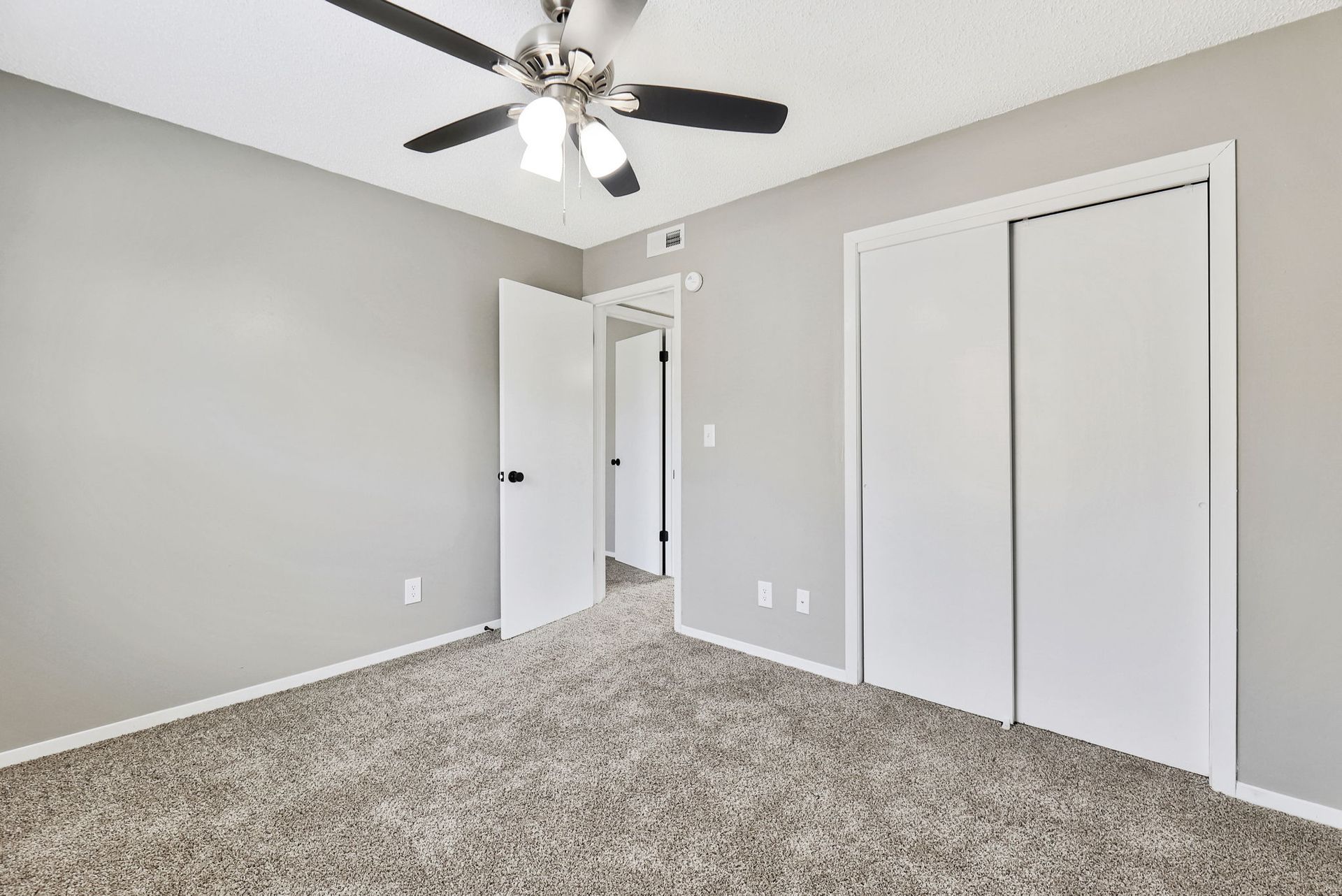 An empty bedroom with a ceiling fan and two closets.