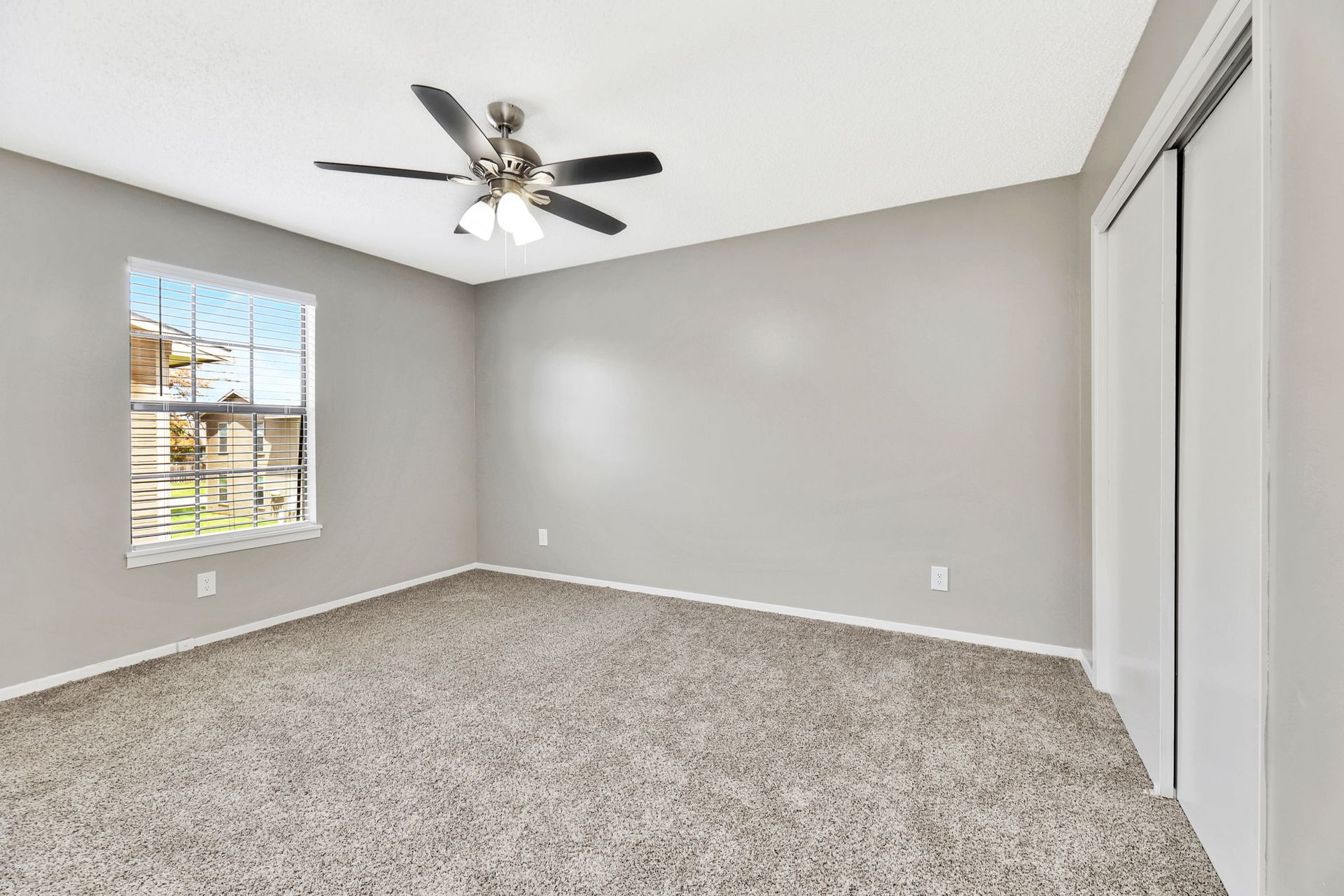 An empty bedroom with a ceiling fan and a window.