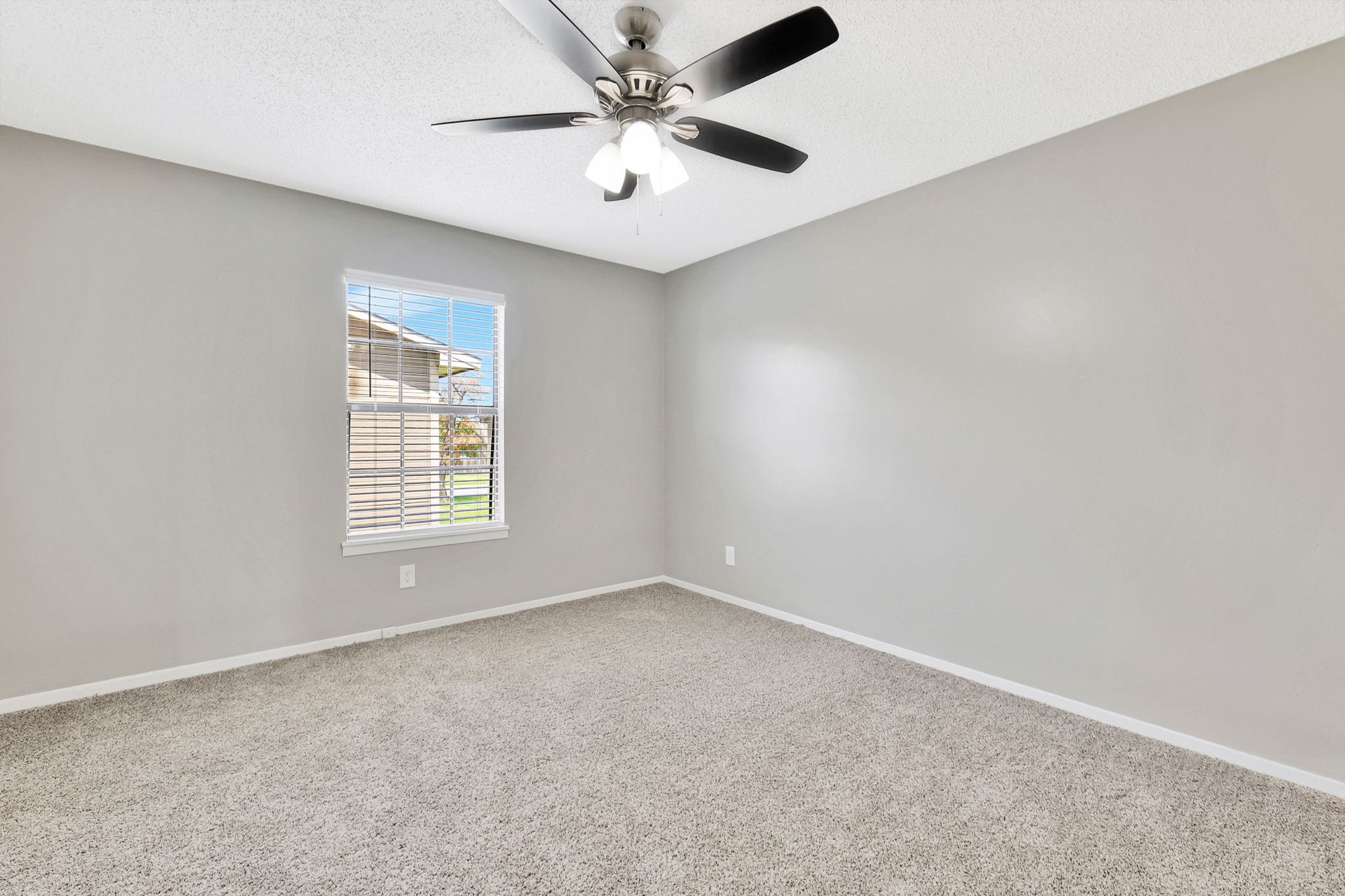 An empty bedroom with a ceiling fan and a window.