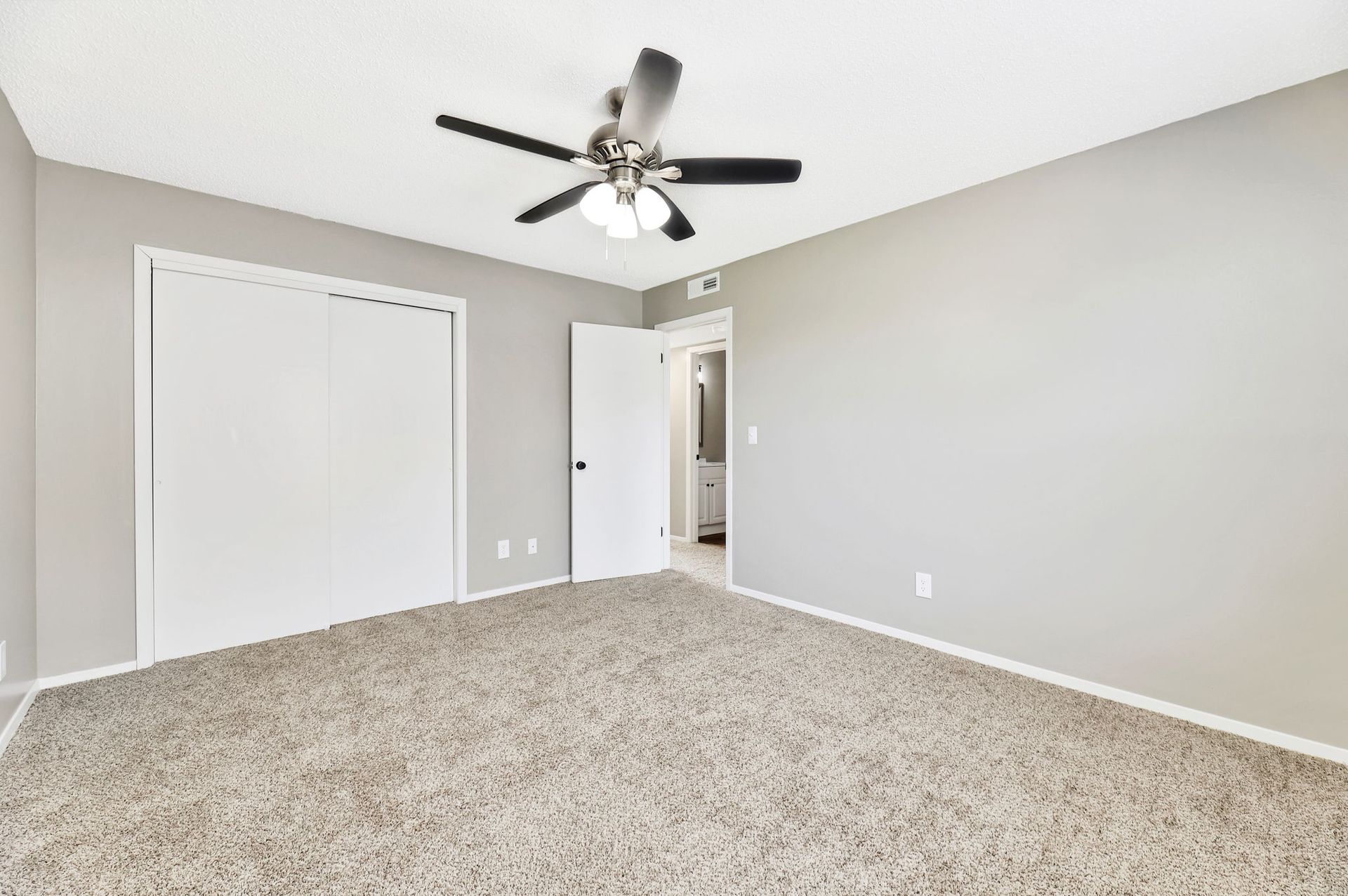 An empty bedroom with a ceiling fan and a carpeted floor.