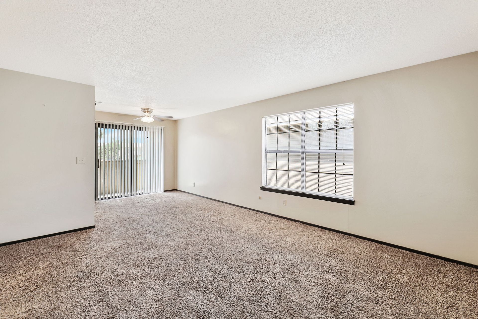 An empty living room with a large window and sliding glass doors.
