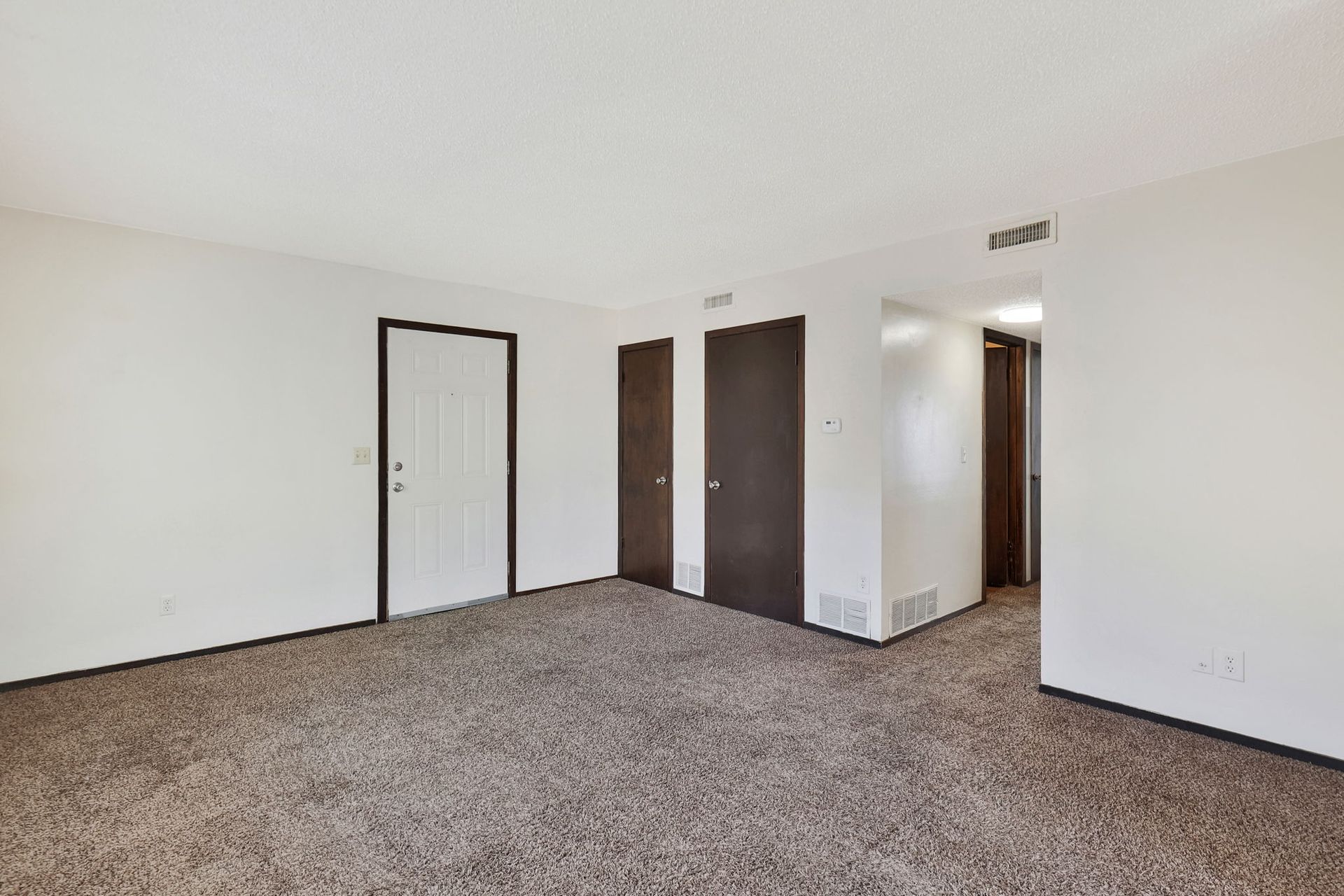An empty living room with a carpeted floor and white walls.