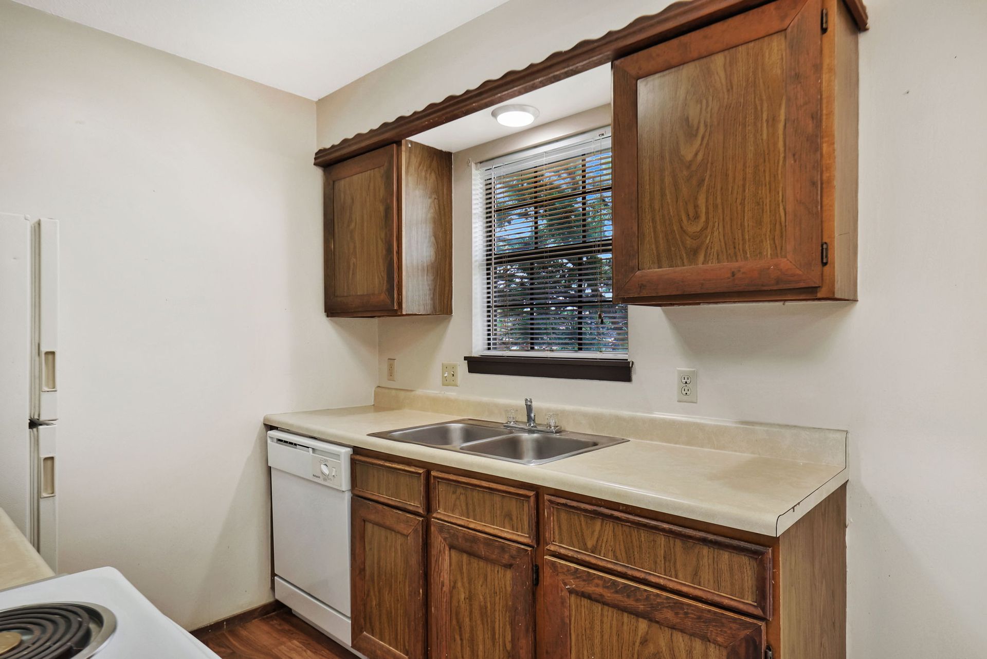 A kitchen with wooden cabinets , a sink , a dishwasher , and a window.