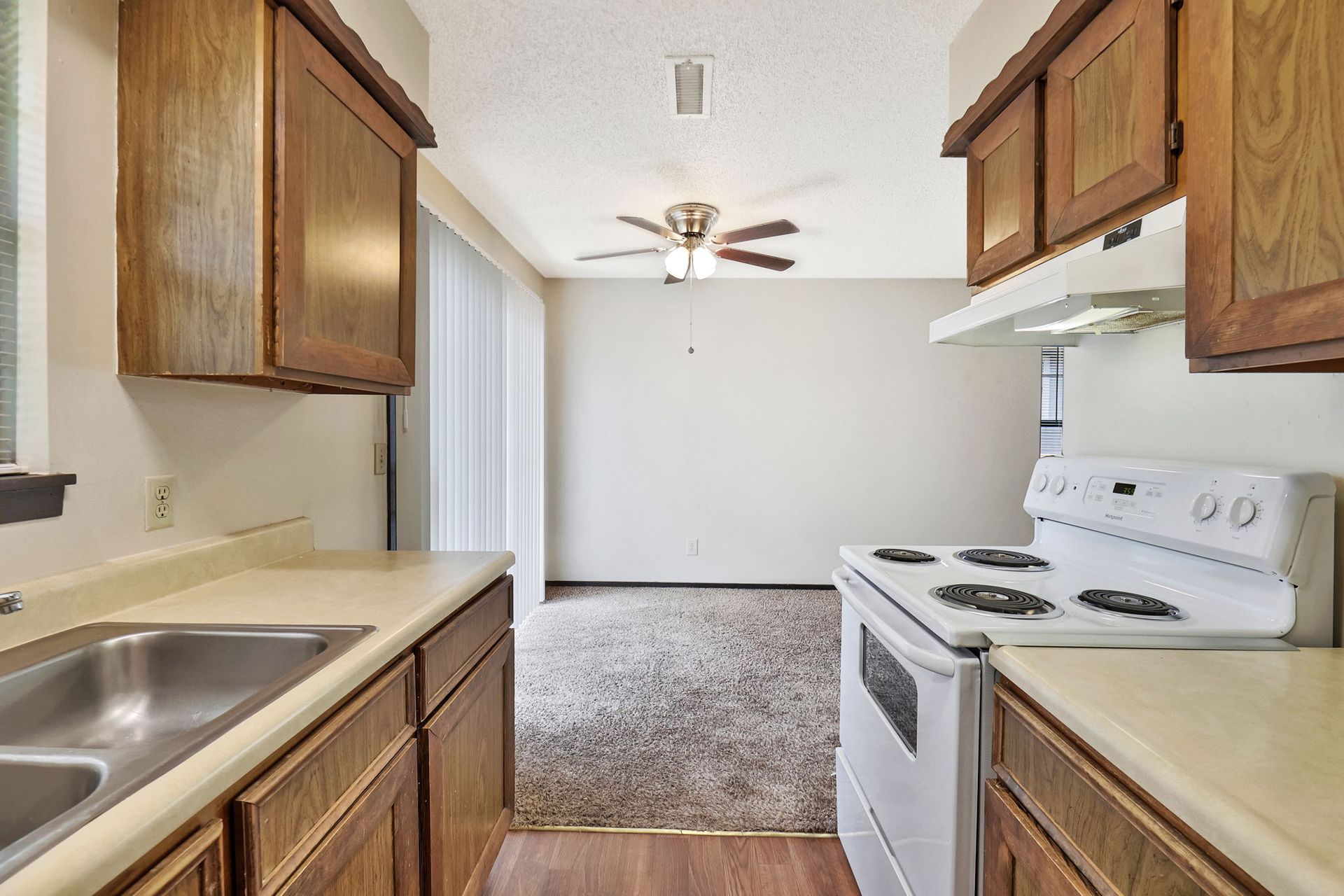 A kitchen with a stove , sink , cabinets and a ceiling fan.