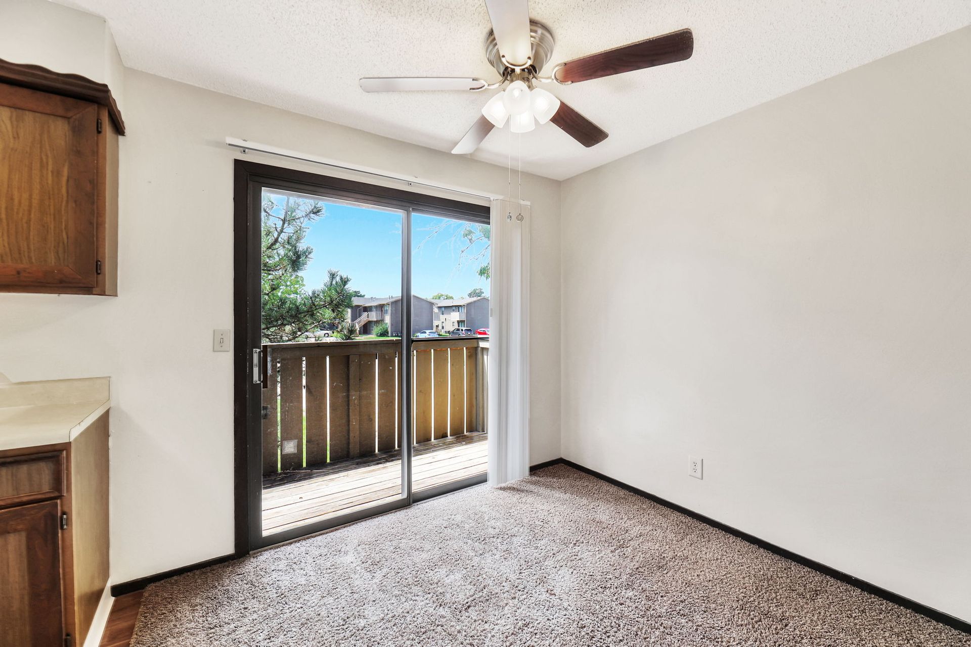 An empty room with a ceiling fan and sliding glass doors leading to a balcony.