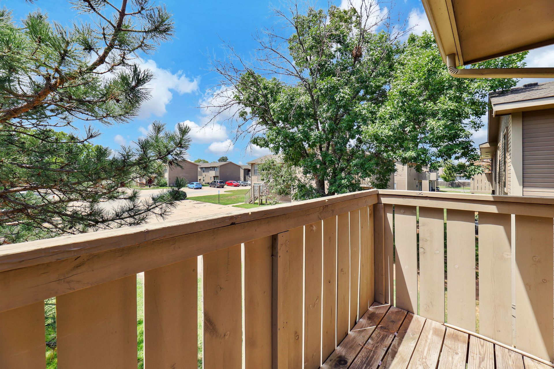 A balcony with a wooden railing and trees in the background.