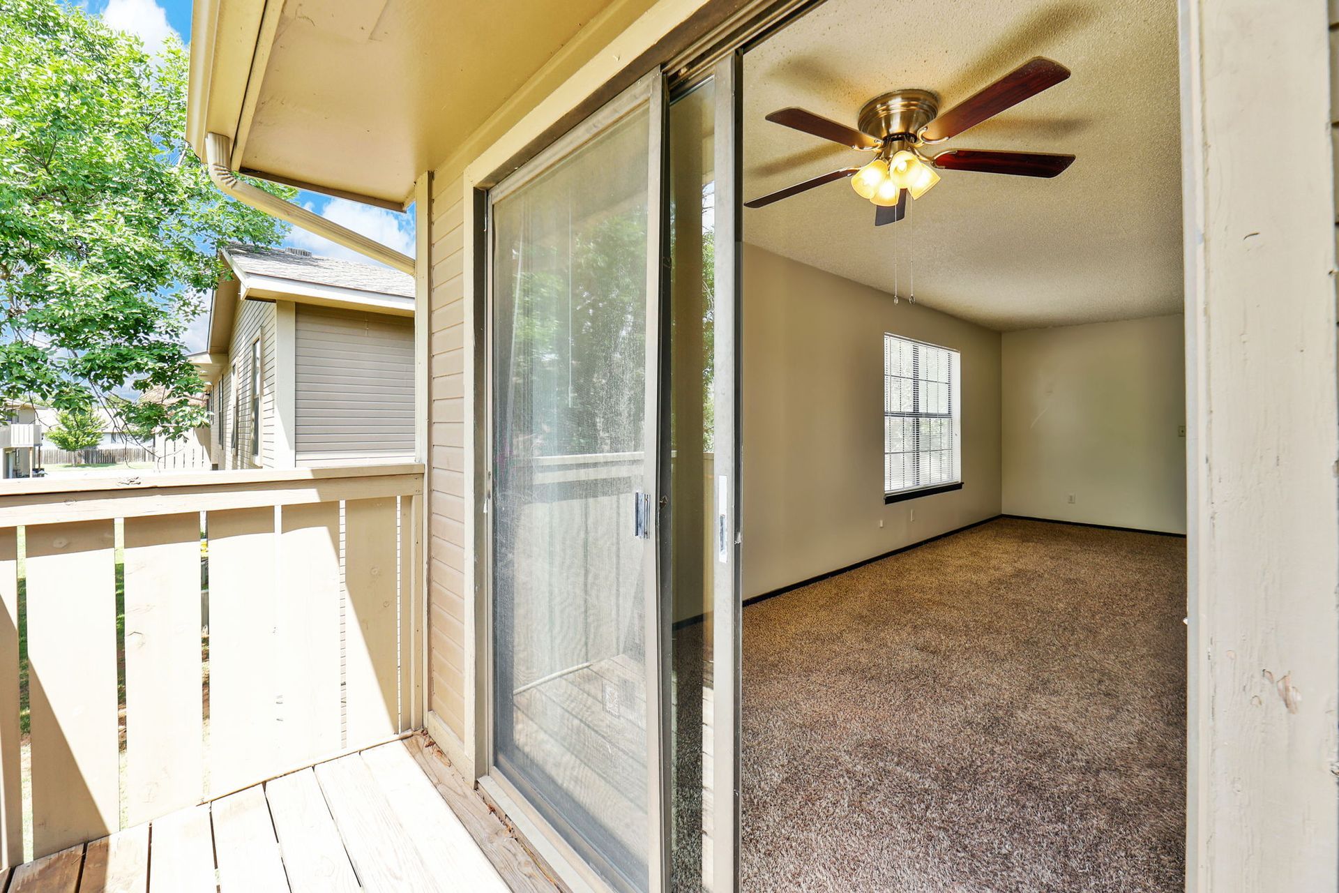 An empty apartment with a sliding glass door and a ceiling fan.