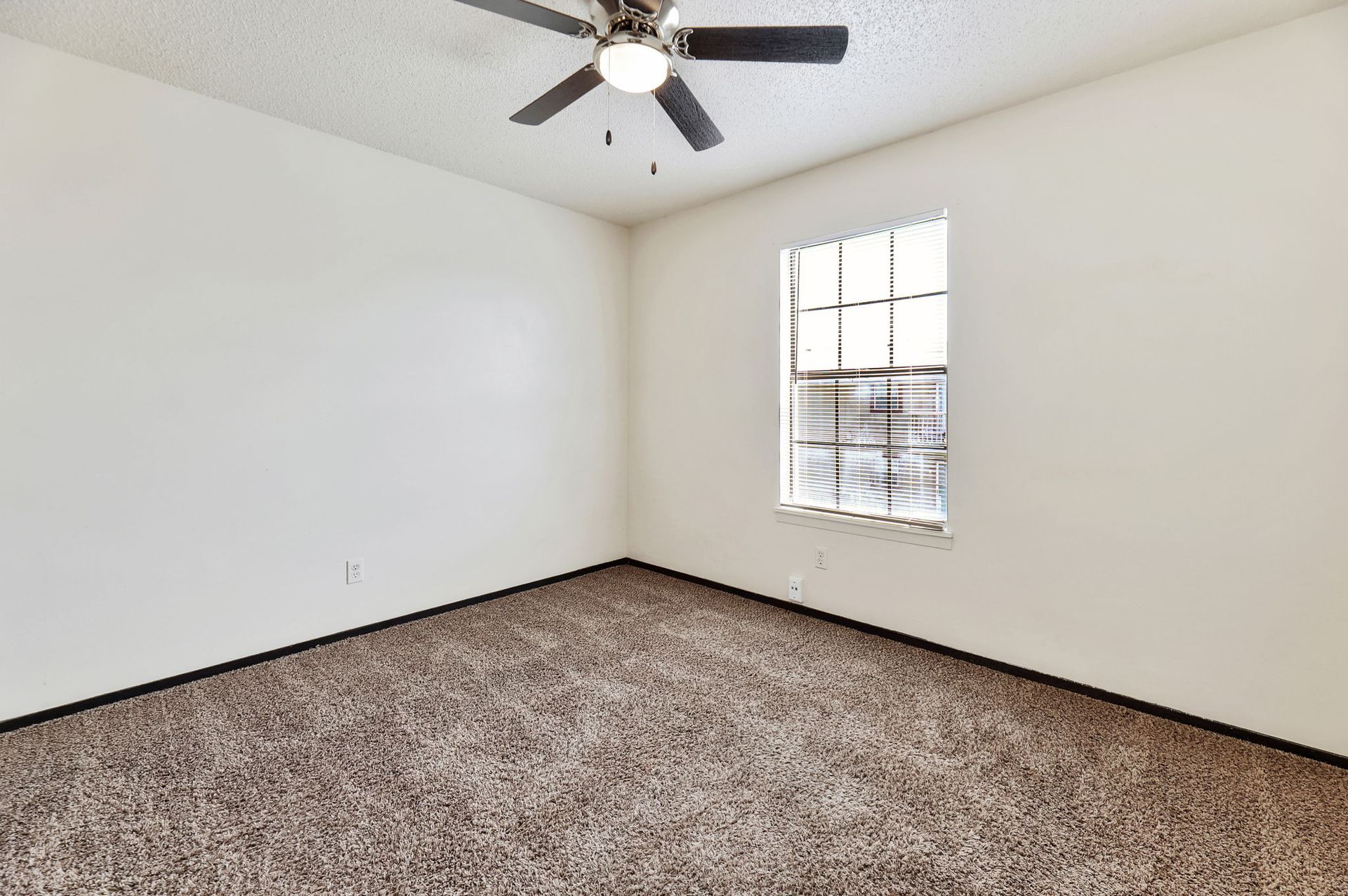An empty bedroom with a ceiling fan and a window.