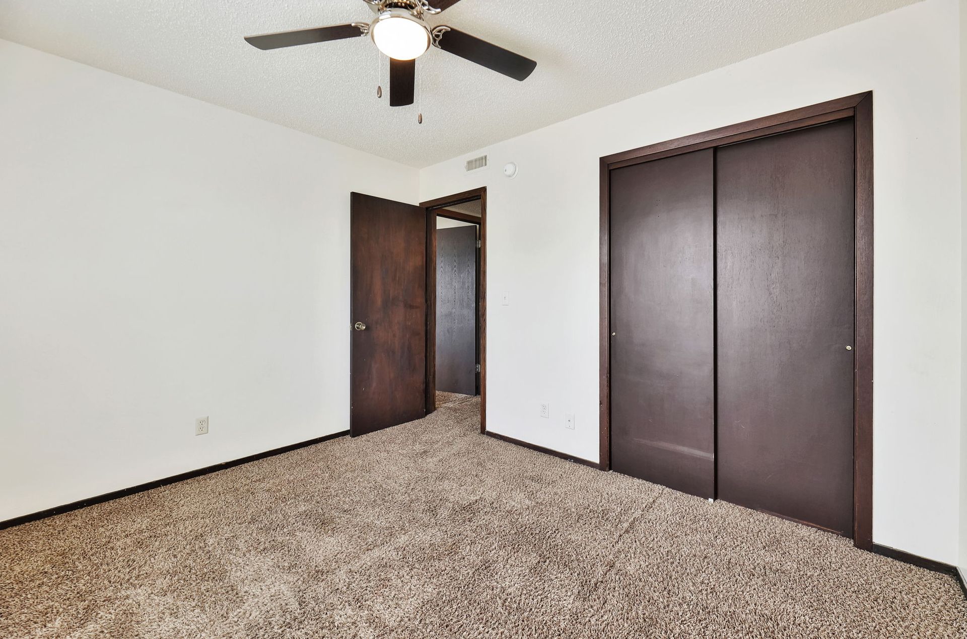 An empty bedroom with a ceiling fan and closets