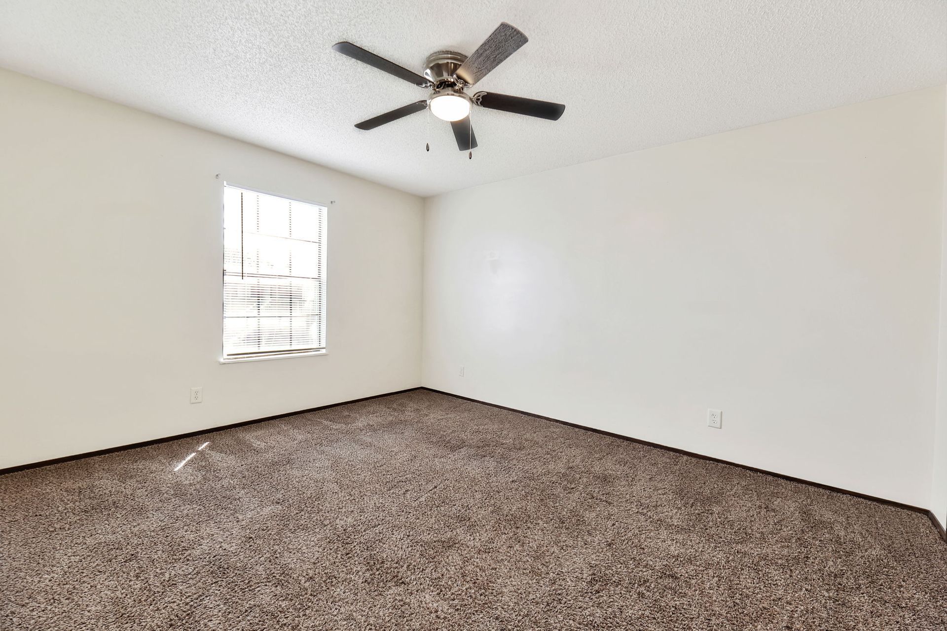 An empty bedroom with a ceiling fan and a window.