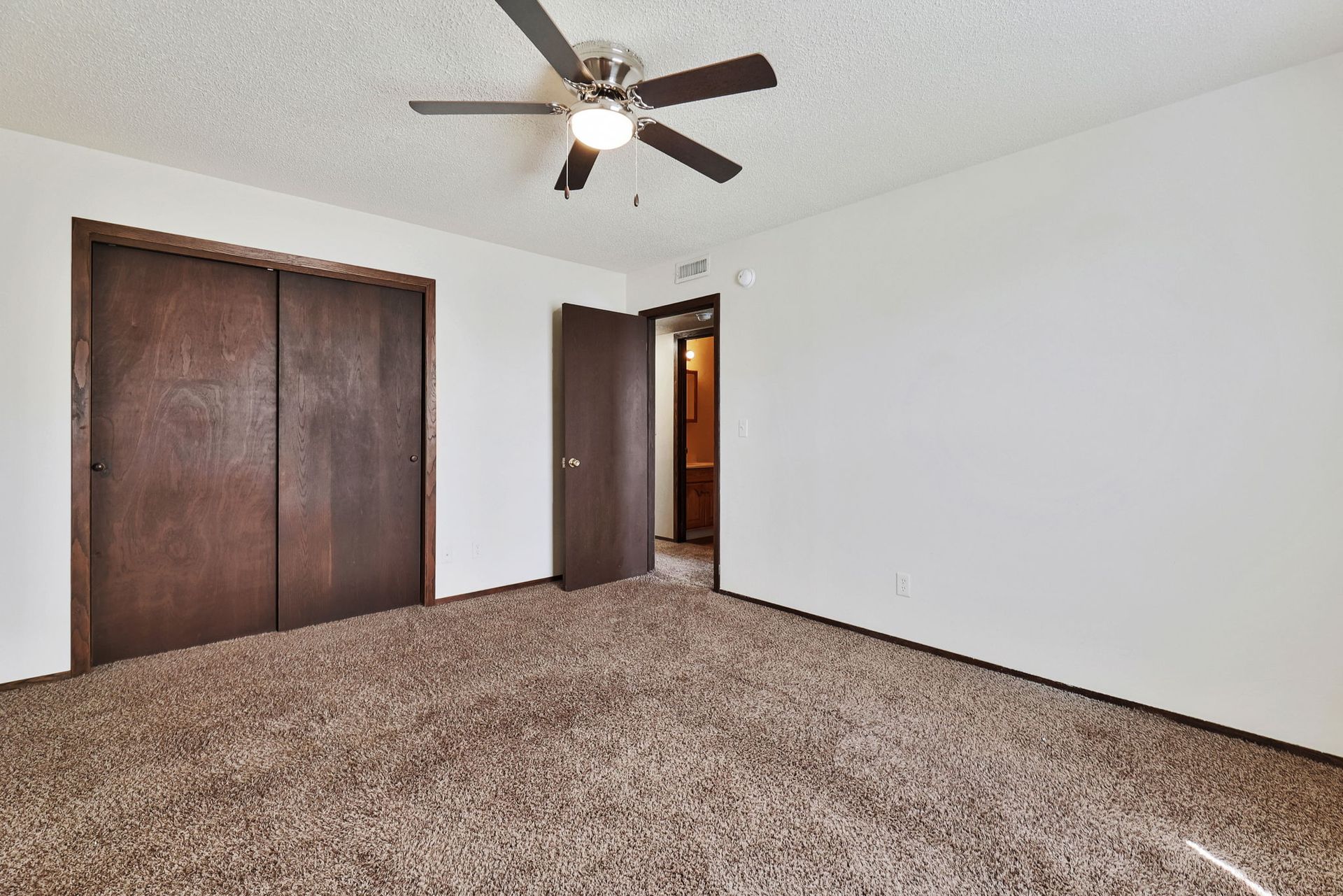 An empty bedroom with a ceiling fan and a closet.