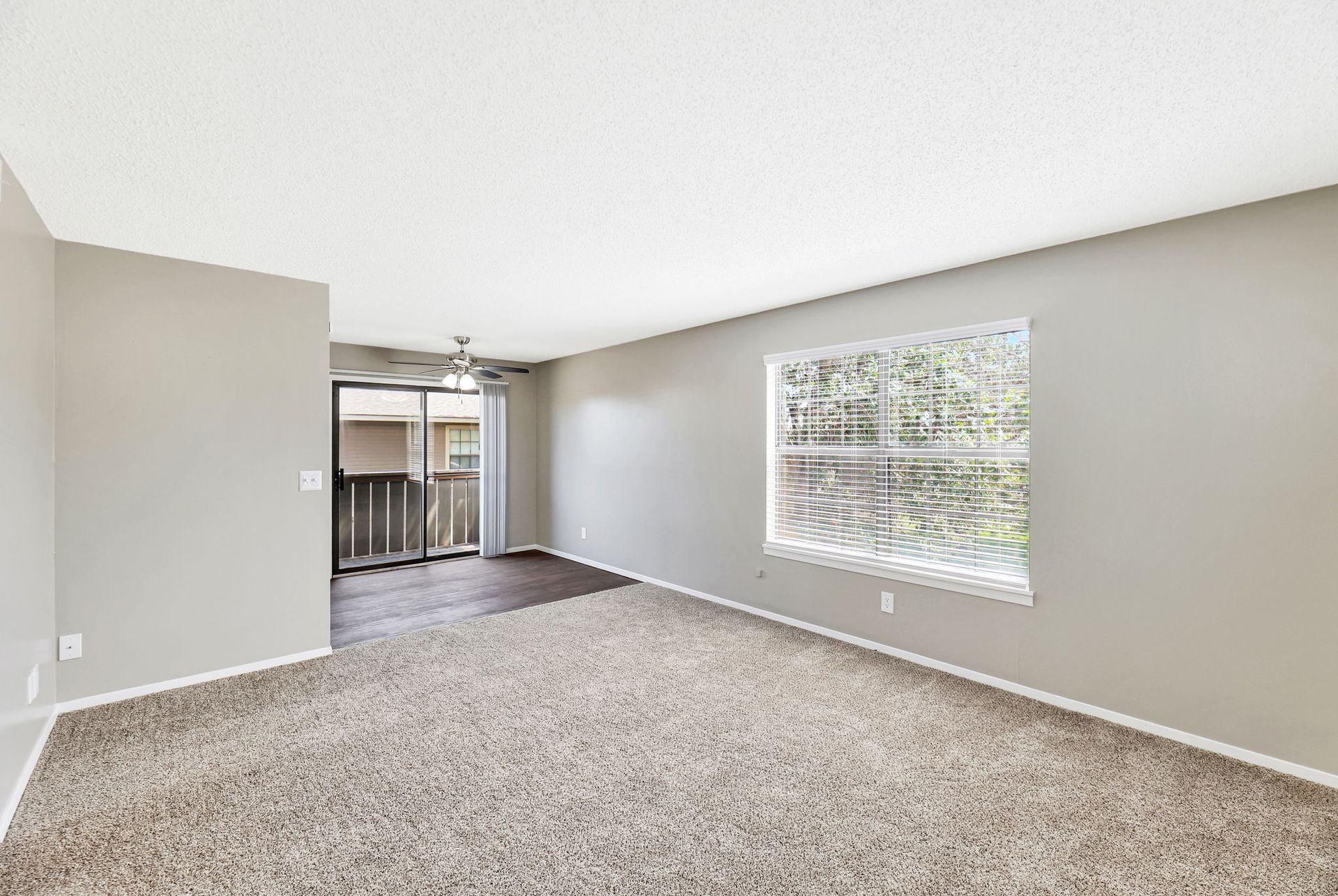 An empty living room with a large window and sliding glass doors.