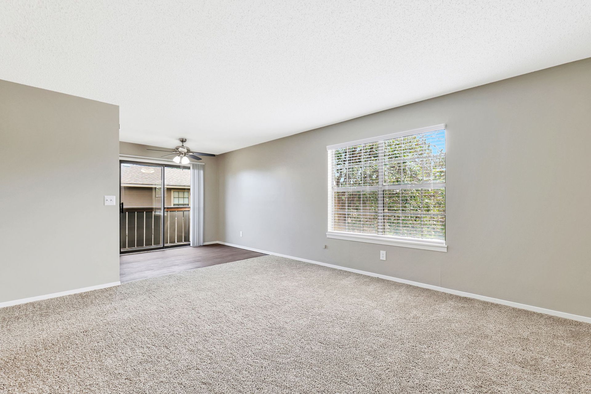 An empty living room with a large window and sliding glass doors.