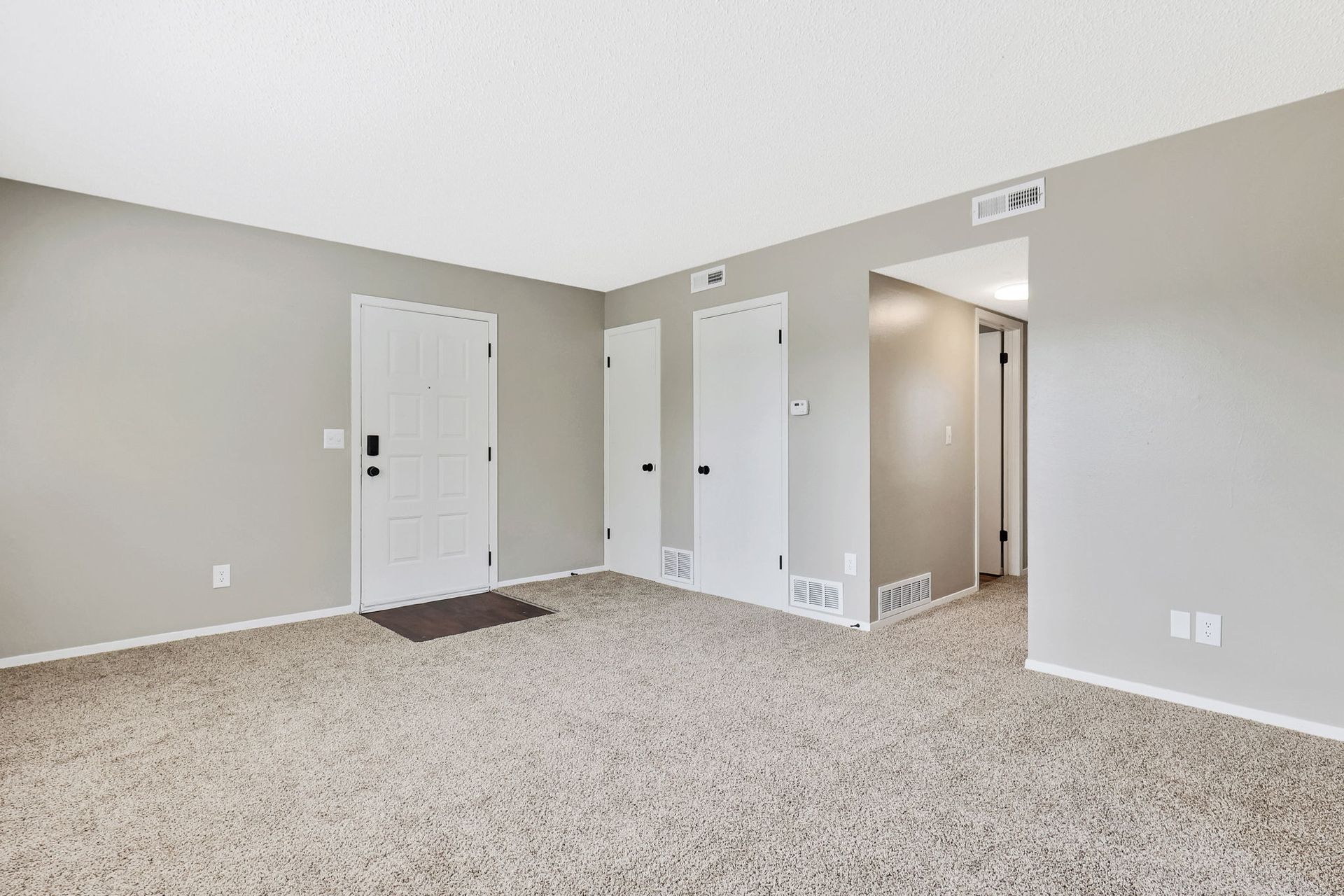 An empty living room with a carpeted floor , gray walls and white doors.