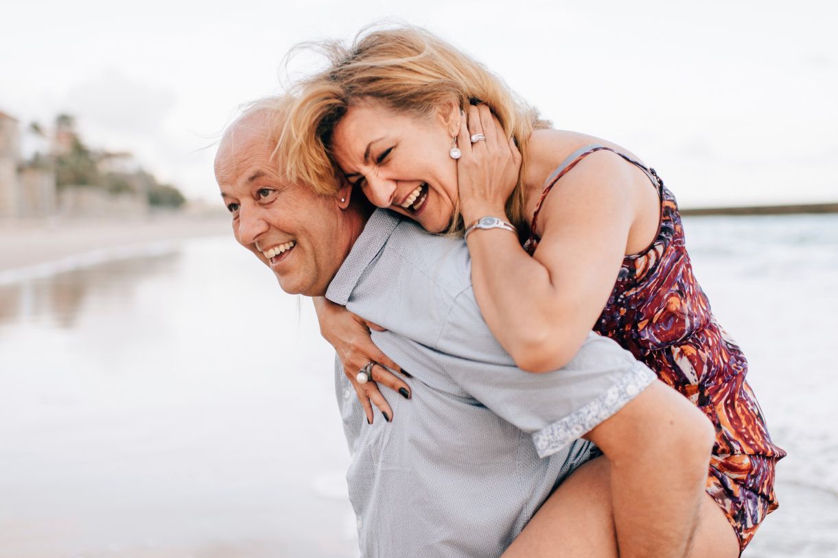A man is carrying a woman on his back on the beach.