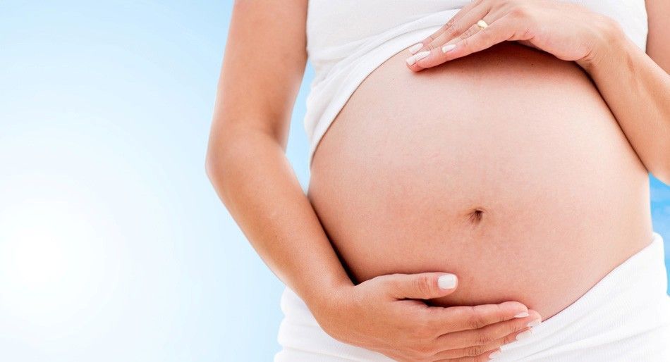 Donna incinta in abito bianco, che culla la pancia, su uno sfondo sfumato blu e bianco.