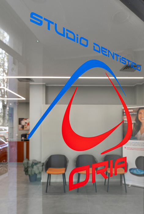 Porta a vetri di uno studio dentistico con logo blu e rosso, sedie visibili nella sala d'attesa.
