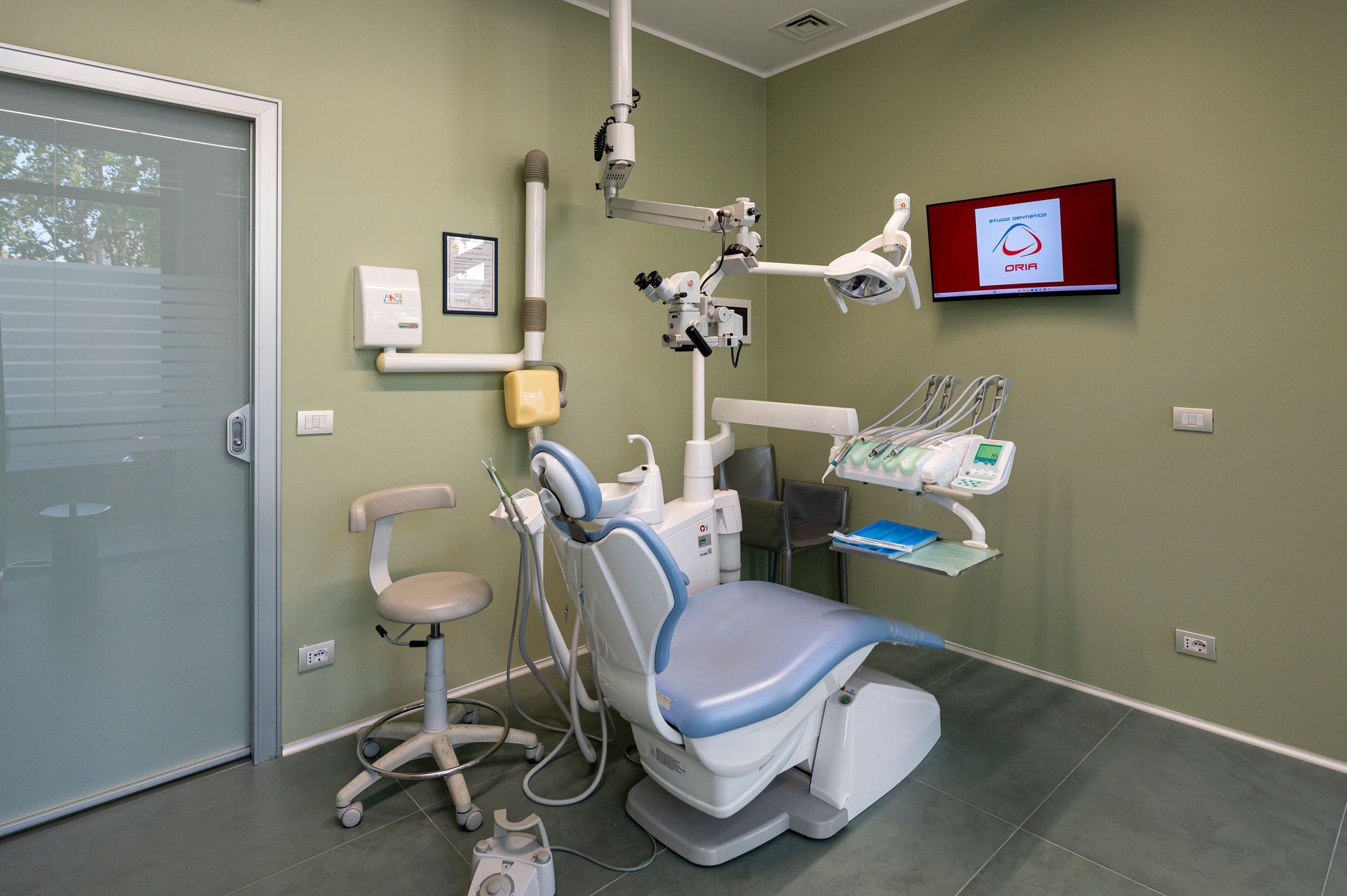 Sala visita odontoiatrica con poltrona, strumenti e schermo montato.
