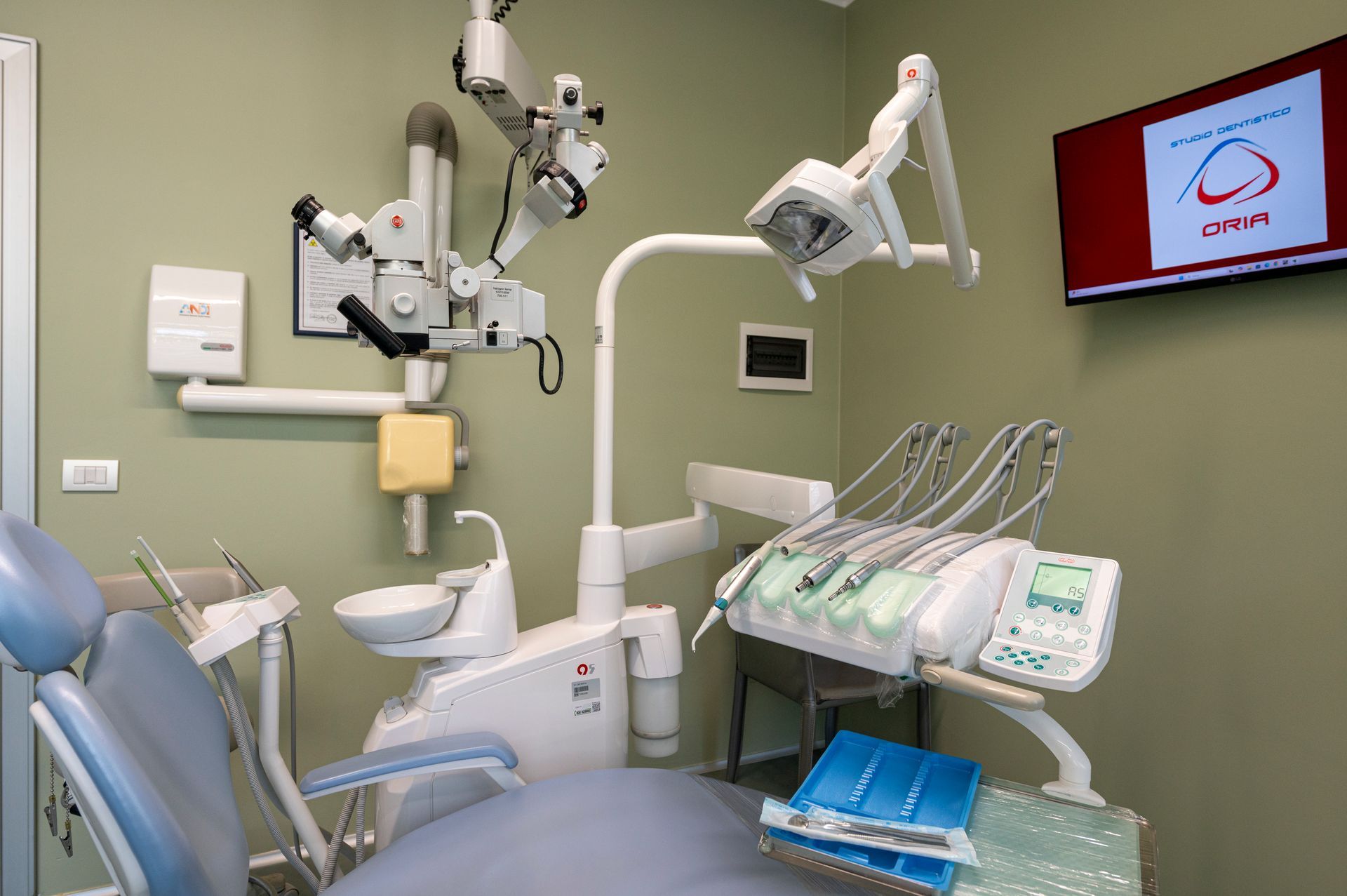 Studio dentistico dotato di attrezzature, tra cui microscopio, poltrona e strumenti.