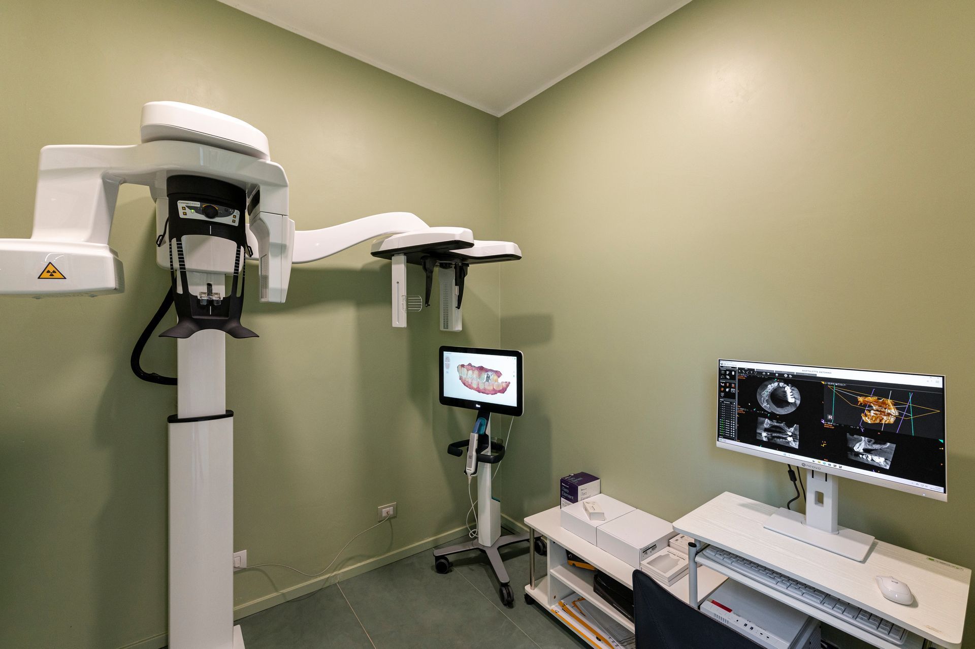 Sala radiologica odontoiatrica con apparecchiature di scansione e monitor per computer su una parete neutra.
