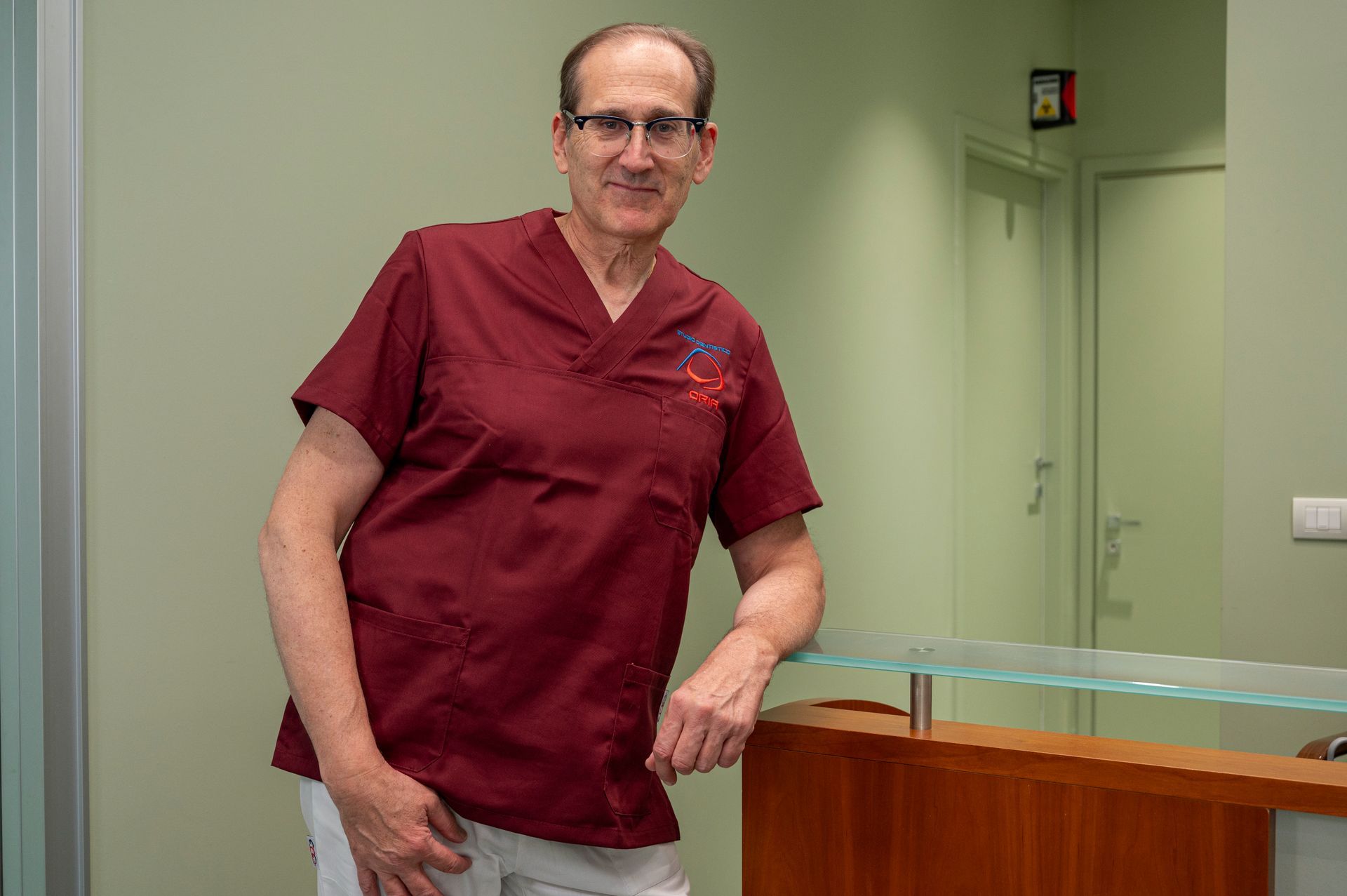 Un uomo in camice color marrone si appoggia alla reception di uno studio medico.