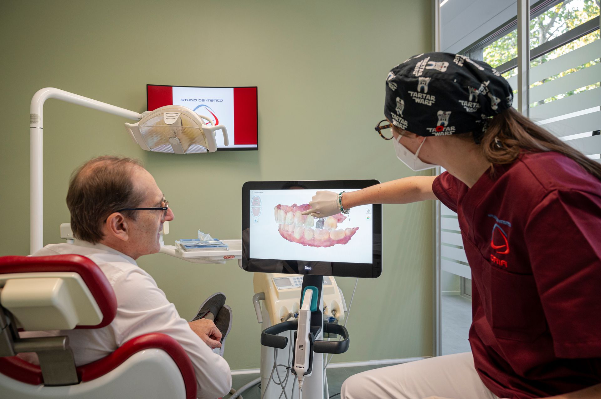 Un dentista mostra a un paziente una scansione dentale digitale su un monitor. Il dentista indica lo schermo.