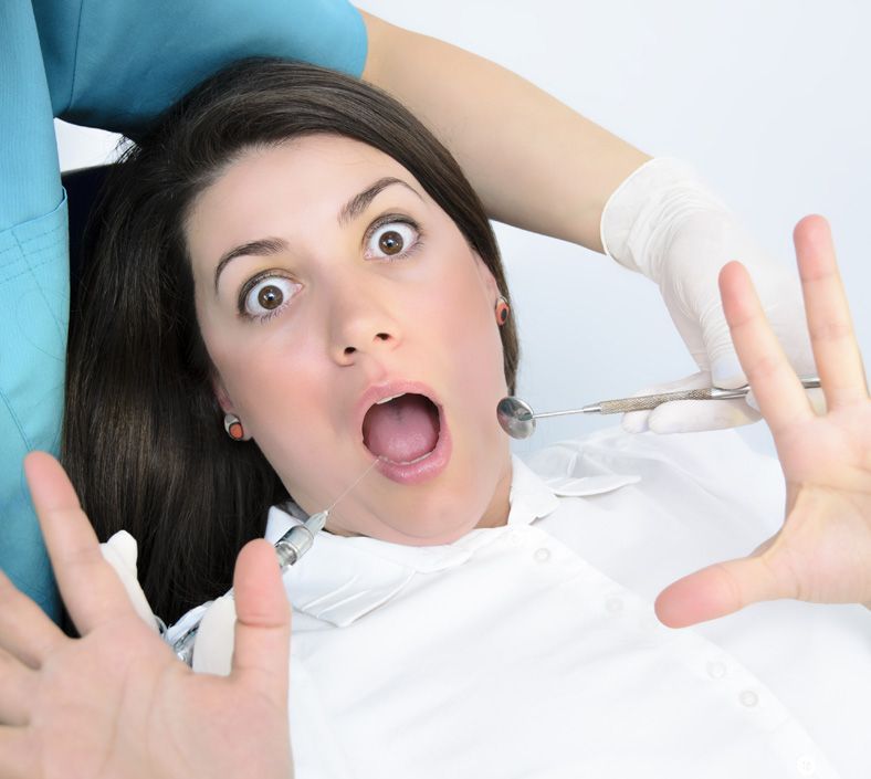 Donna con gli occhi spalancati e la bocca aperta dal dentista, che allunga le braccia. Il dentista tiene in mano degli strumenti.