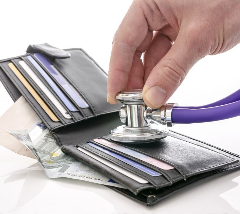 Mano con stetoscopio che esamina un portafoglio con soldi e carte di credito.