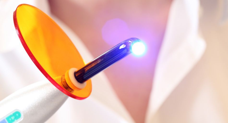 Lampada fotopolimerizzatrice dentale con schermo arancione che emette una luce blu brillante.
