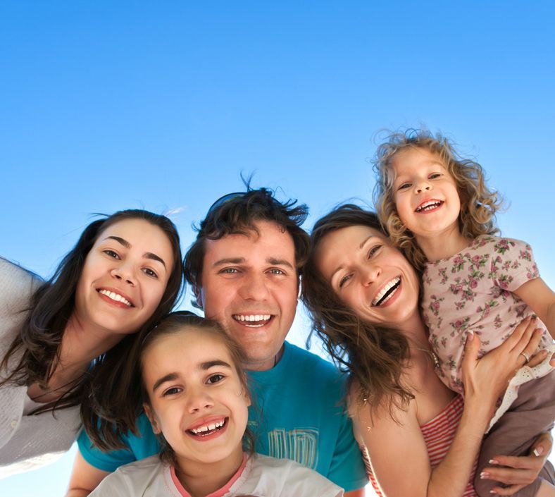 Famiglia di cinque persone che sorride gioiosamente sotto un cielo azzurro.