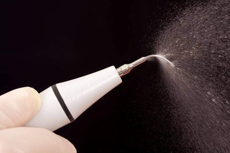 Una mano che tiene uno scaler dentale e spruzza acqua. Sfondo nero.