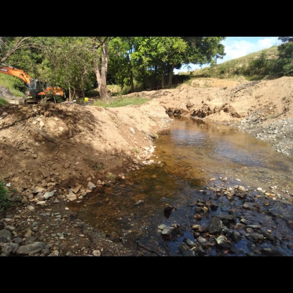 A Large Pile of Dirt is Sitting Next to a River — Gears Excavation In Cedar Pocket, QLD