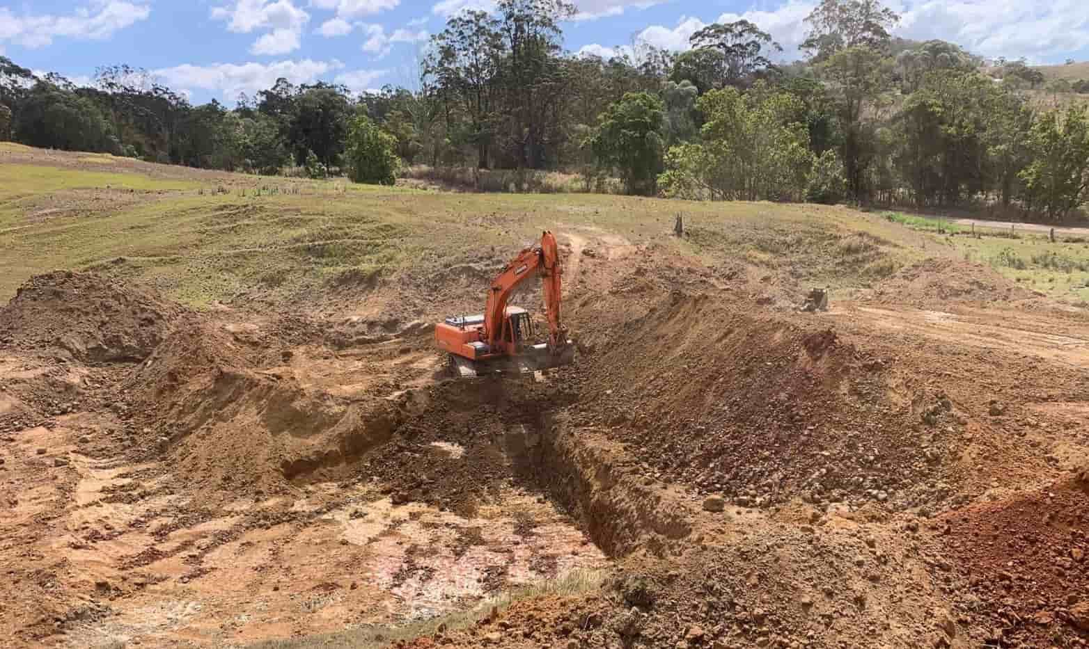 An Excavator is Digging a Hole in the Dirt in a Field — Gears Excavation In Cedar Pocket, QLD