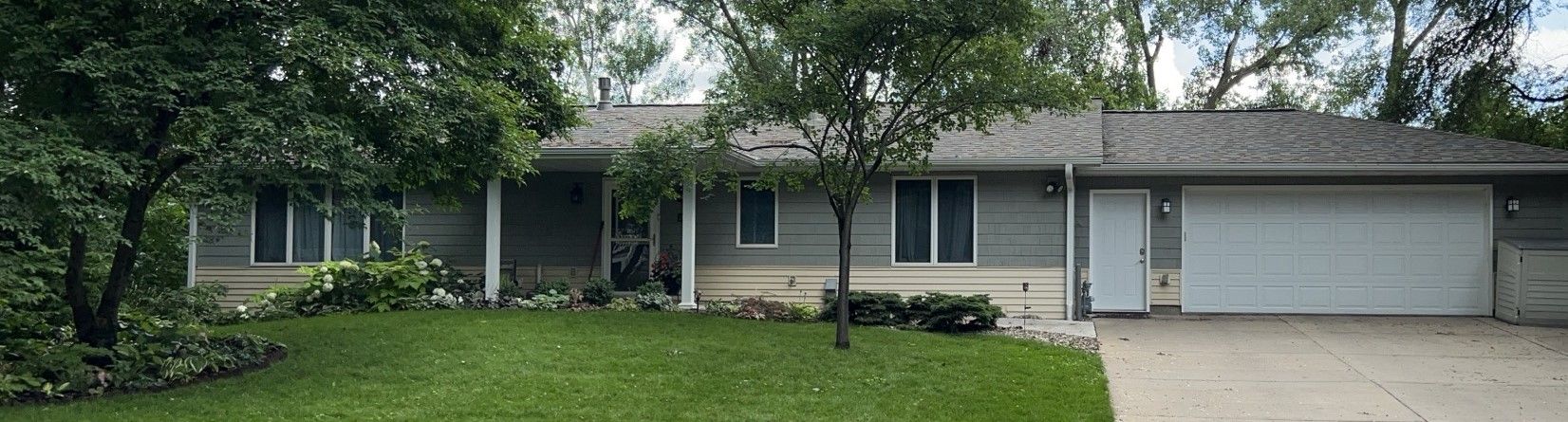 A house with a large garage and a porch surrounded by trees.