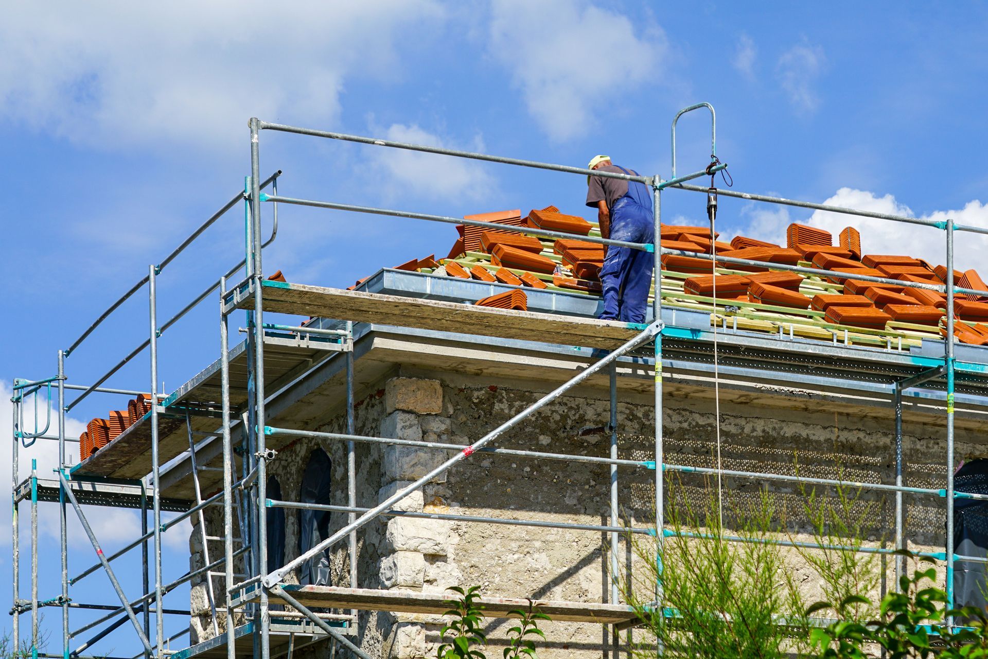 A worker is replacing the clay tile roof covering an old stone house.