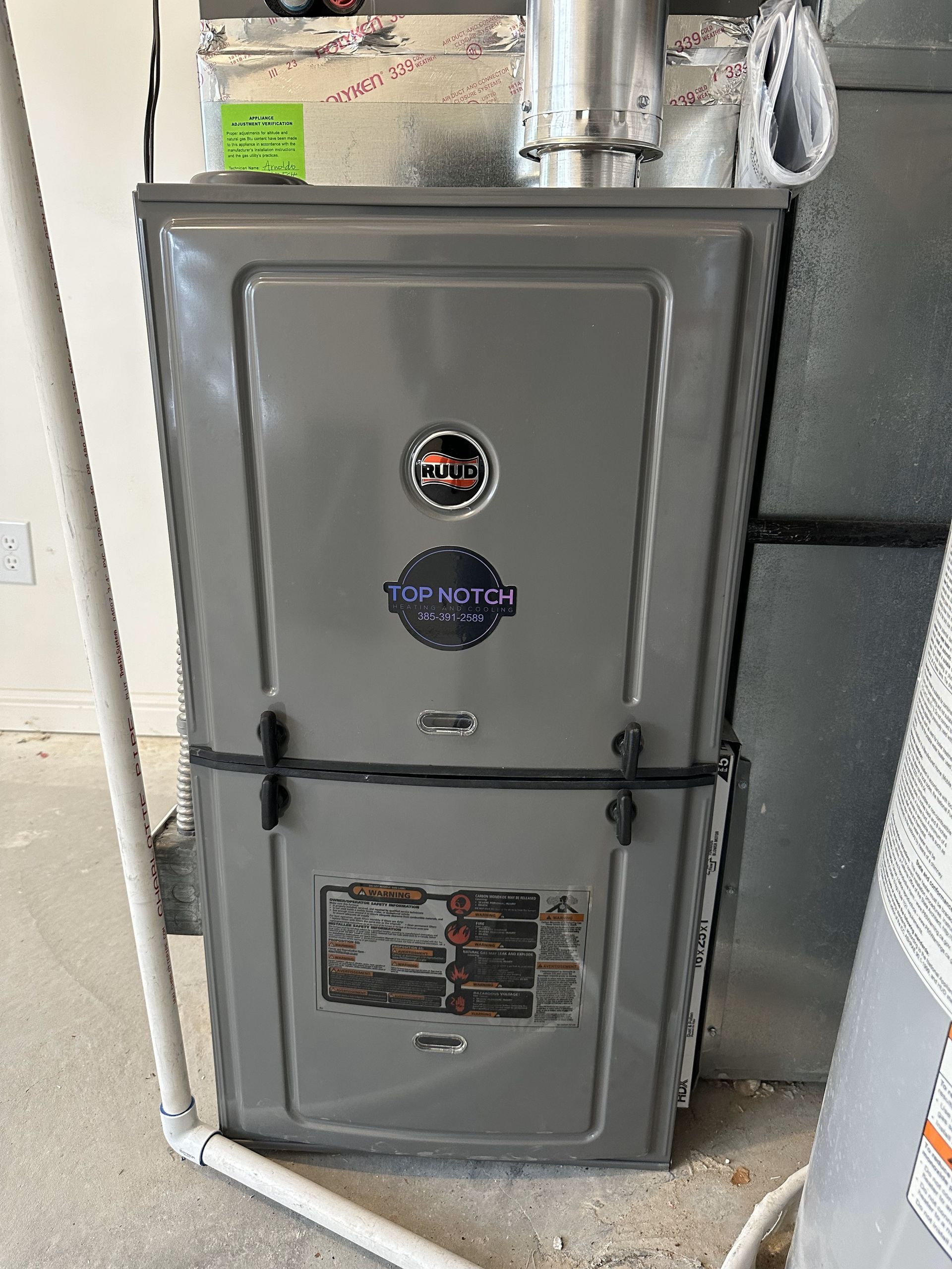 A gray furnace is sitting in a garage next to a water heater.