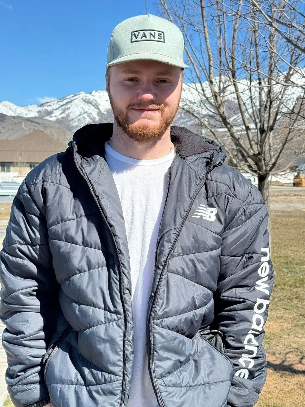 A man wearing a hat and a jacket is standing in front of a mountain.