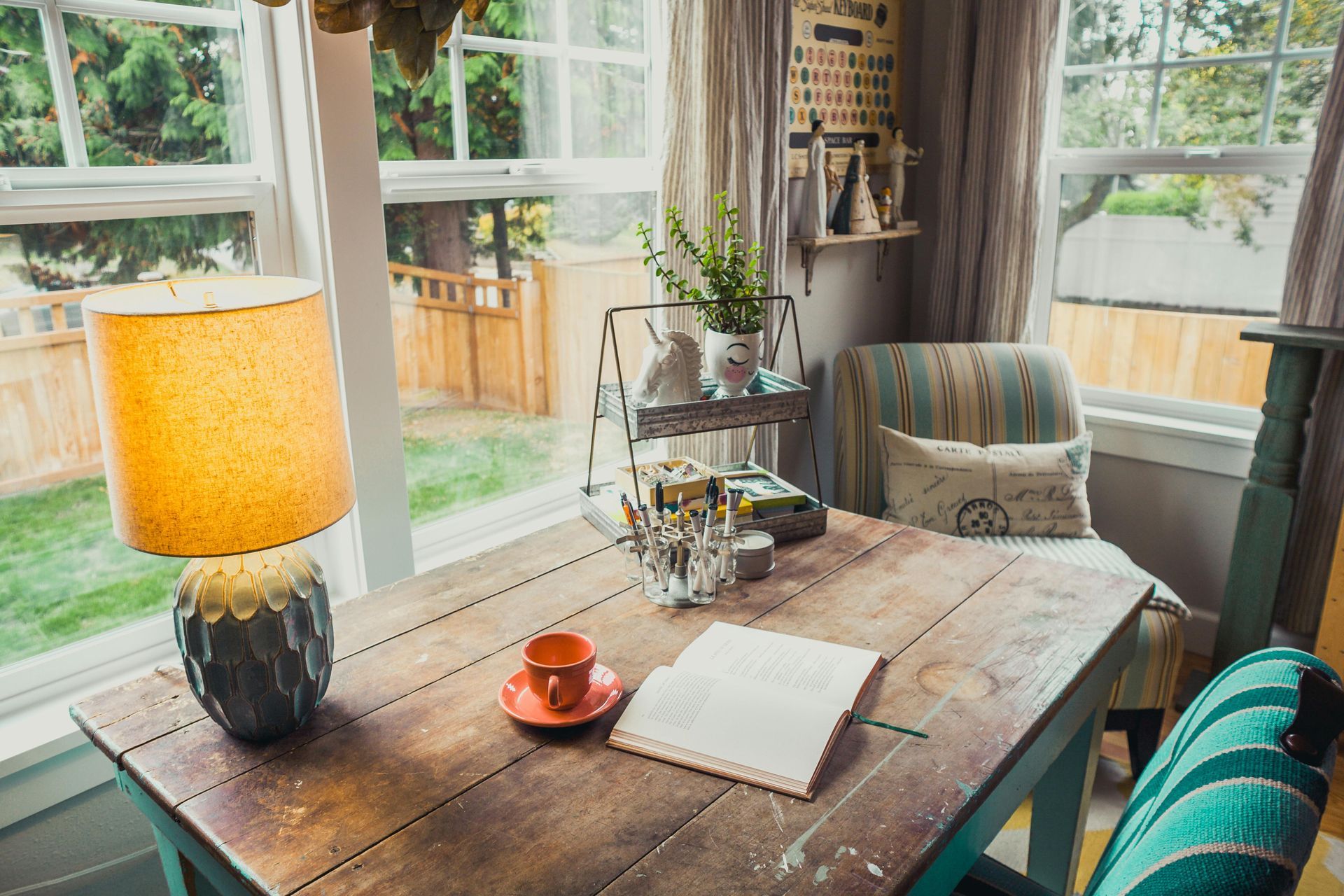 A wooden table with a lamp and a notebook on it in front of a window.