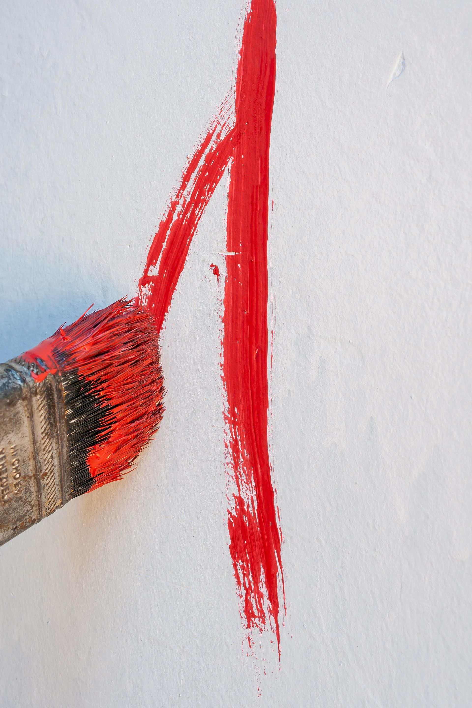 A brush is being used to paint a red line on a white surface