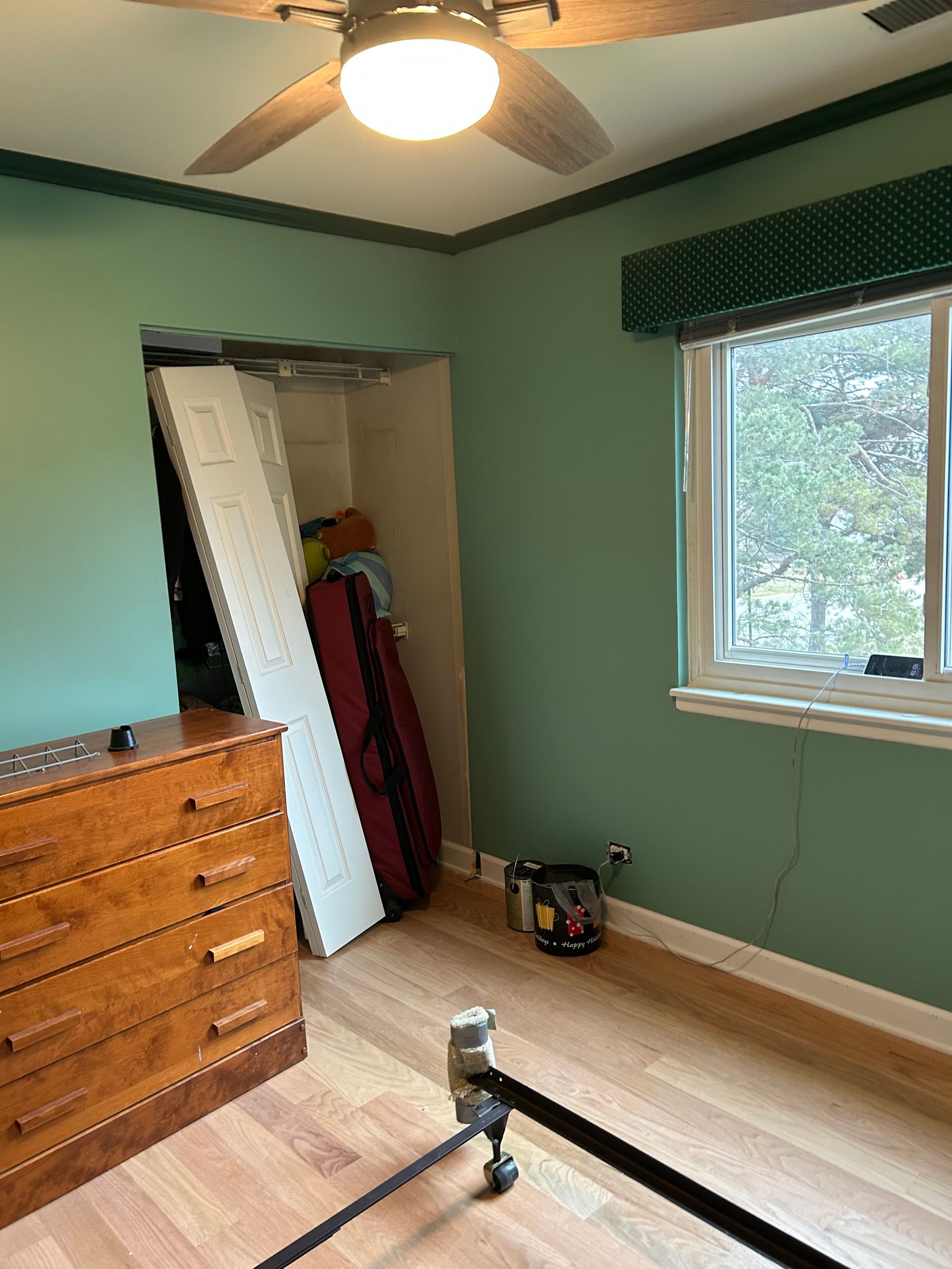 Bedroom with green walls, wooden floor, closet, dresser, window, and ceiling fan.