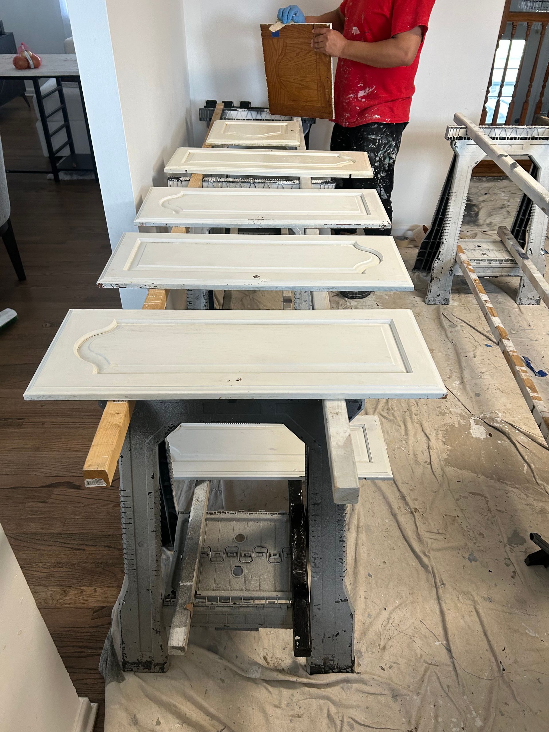 Person painting cabinet doors outdoors; light gray, on sawhorses.