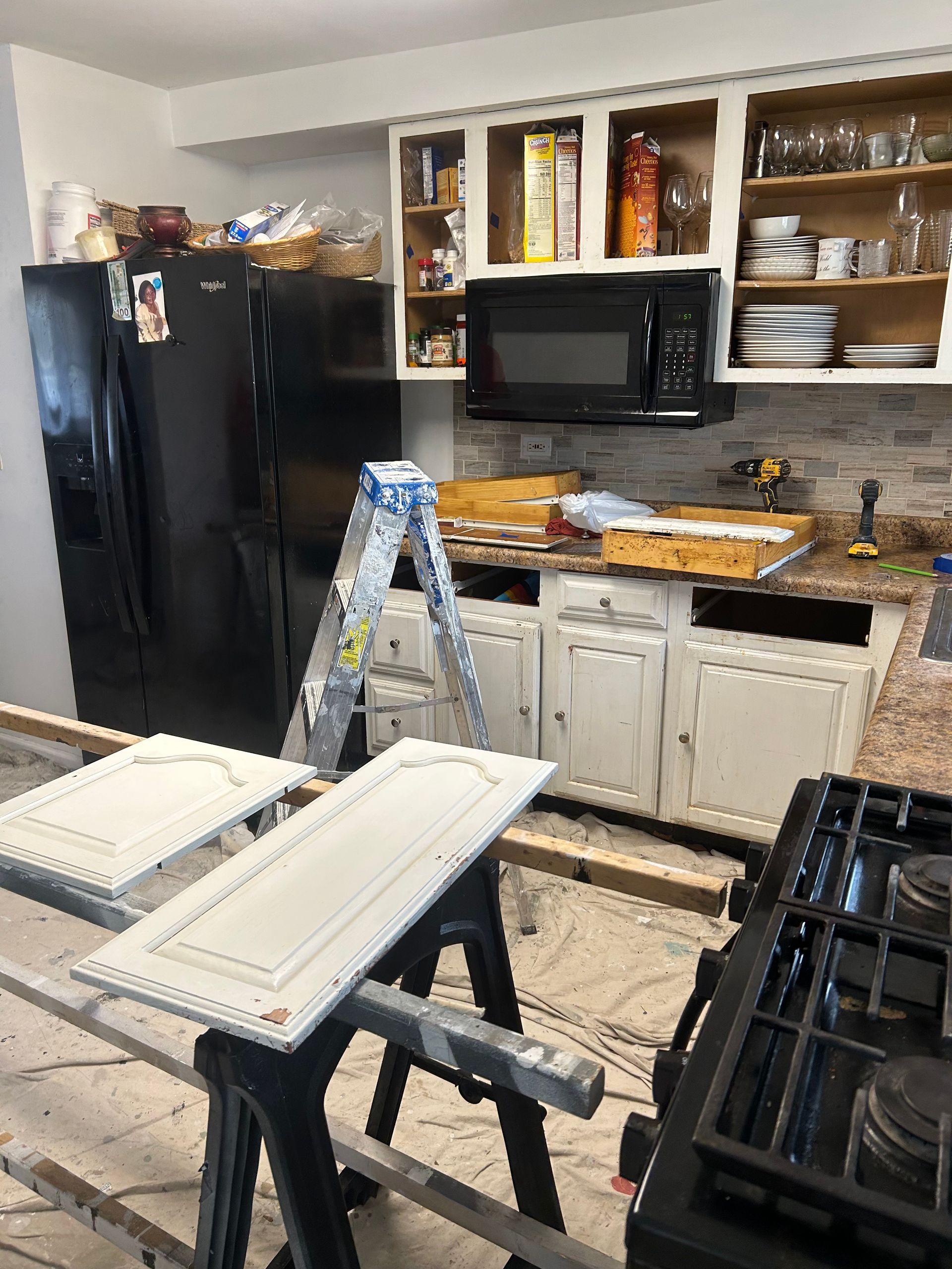 Kitchen under renovation with cabinets, appliances, and tools.