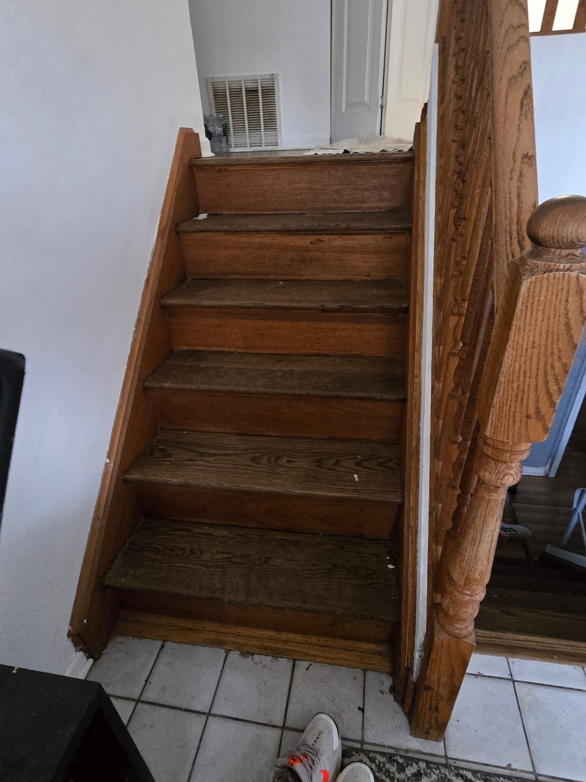 Wooden staircase with worn steps; a banister is on the right, tiled floor below.